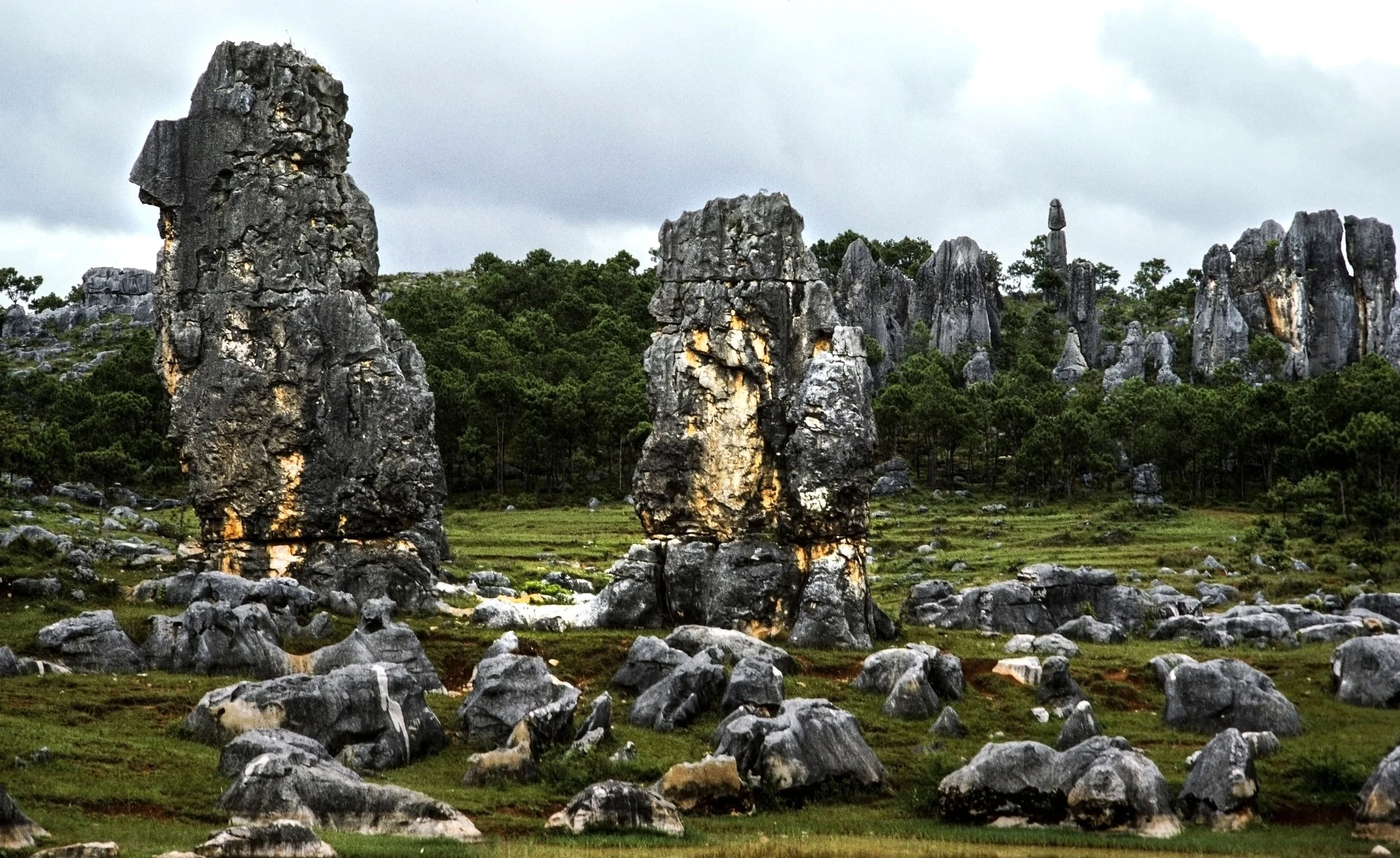 A landscape of large limestone rock formations and green vegetation under a cloudy sky.