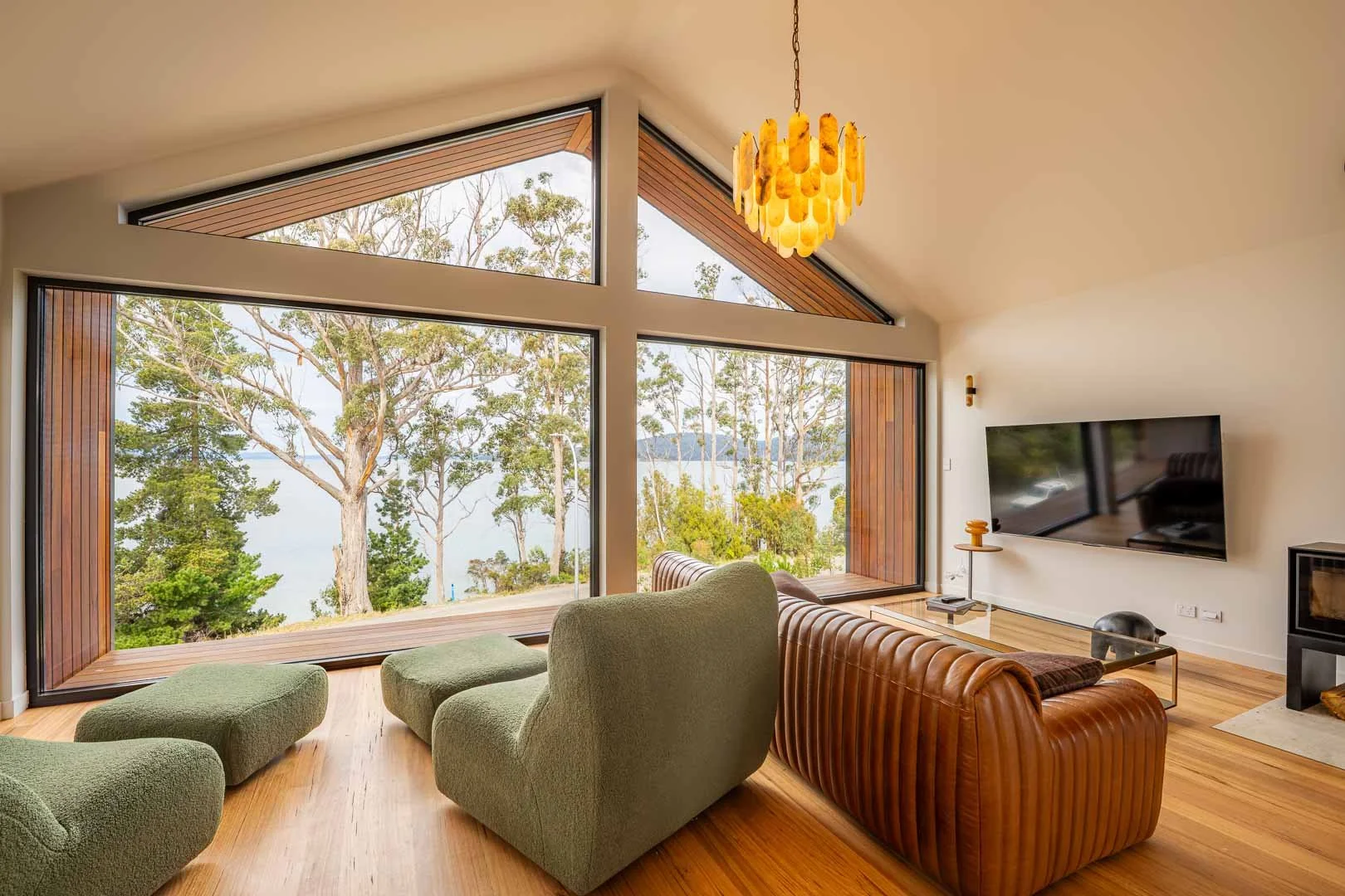 Modern living room with large windows overlooking trees and a body of water, featuring professional electrical fitout