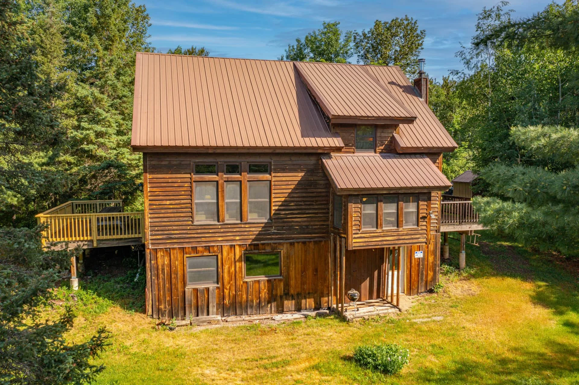 A wooden house with a metal roof surrounded by green trees and grass.