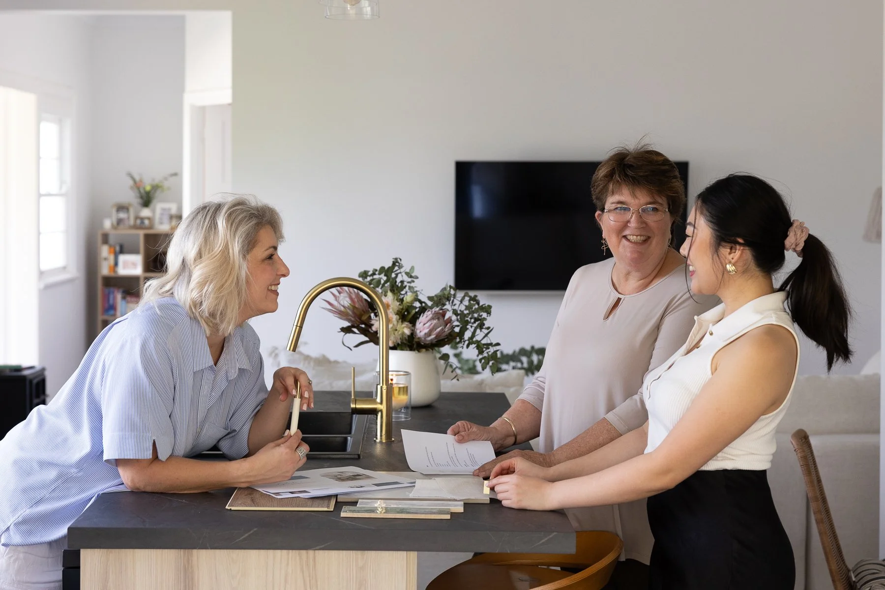 Property Renovation Experts, Lisa and Sue in their clients freshly renovated and stylish kitchen. They are smiling and looking at the renovation plans for the project.