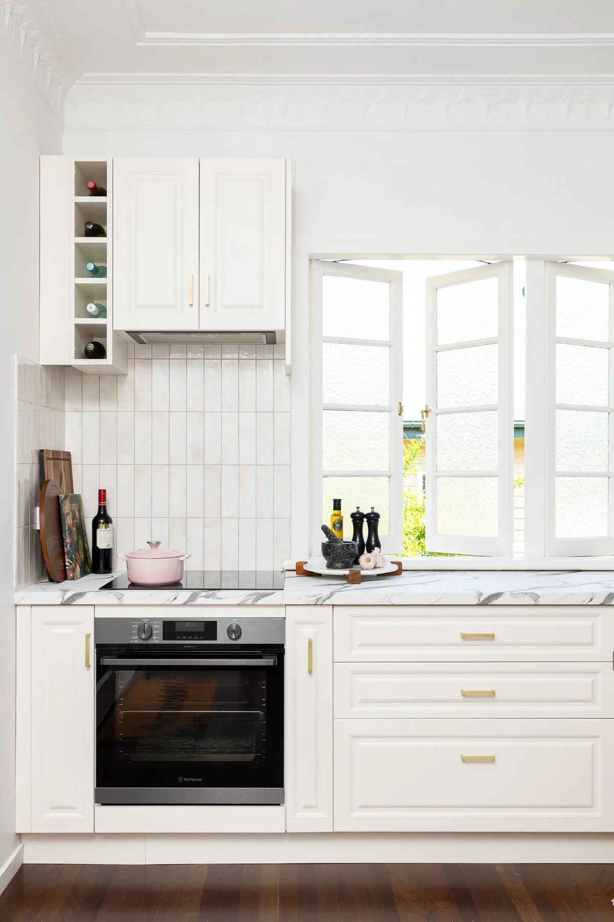 White kitchen with window, wine bottles, cooking pot, and kitchen tools.