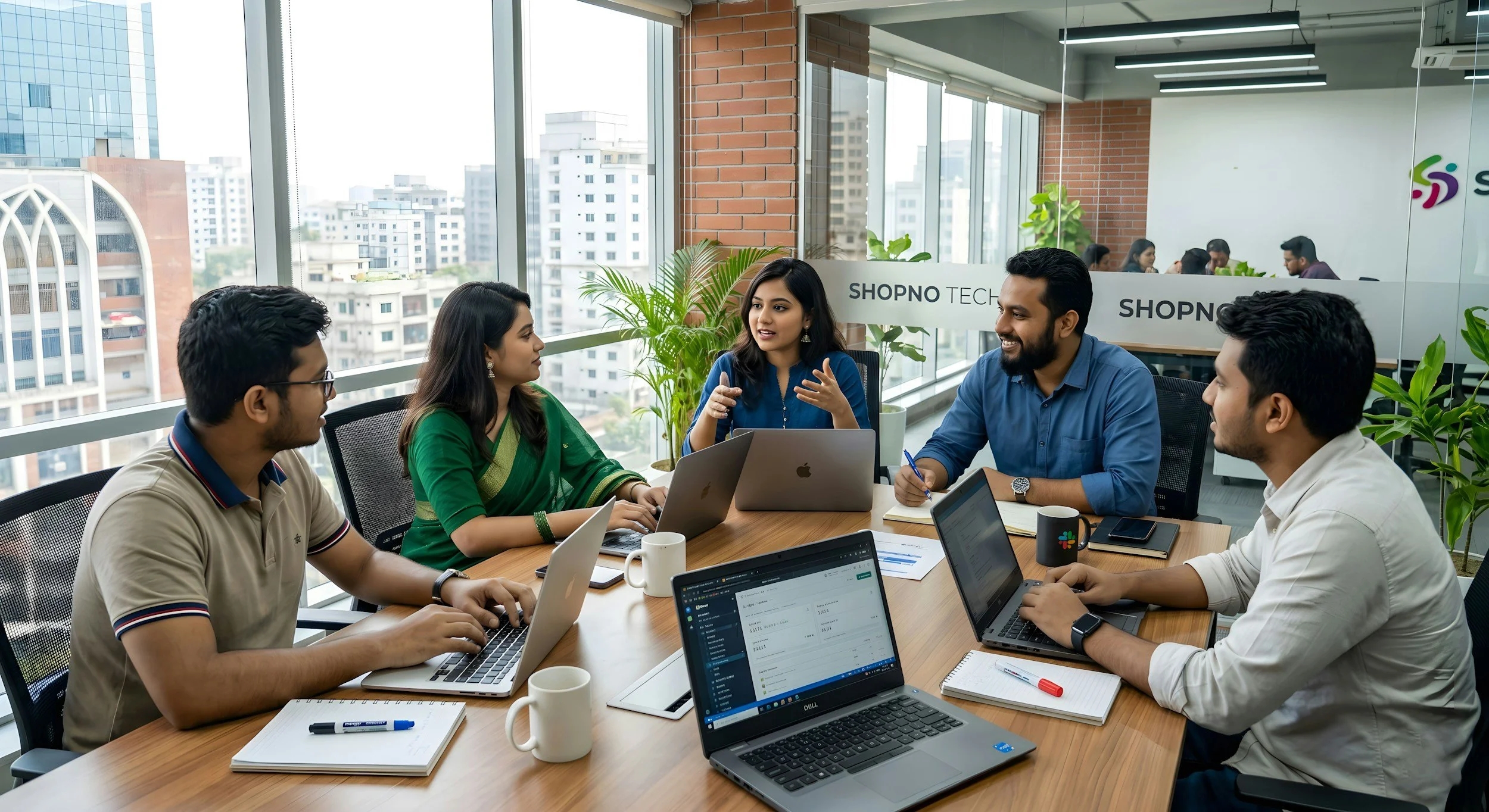 A diverse group of six people having a meeting in a modern office with large windows, laptops, notebooks, and coffee mugs, engaged in a discussion.