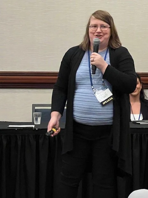 Michelle Pezley speaking at a conference, wearing a badge with 'SPEAKER' on it.
