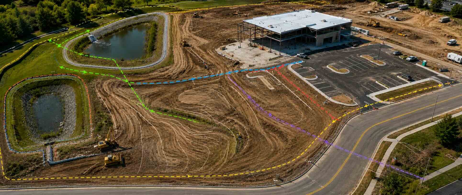 Aerial construction site showing civil engineering features, grading, drainage ponds, utility routes, parking, and site access.