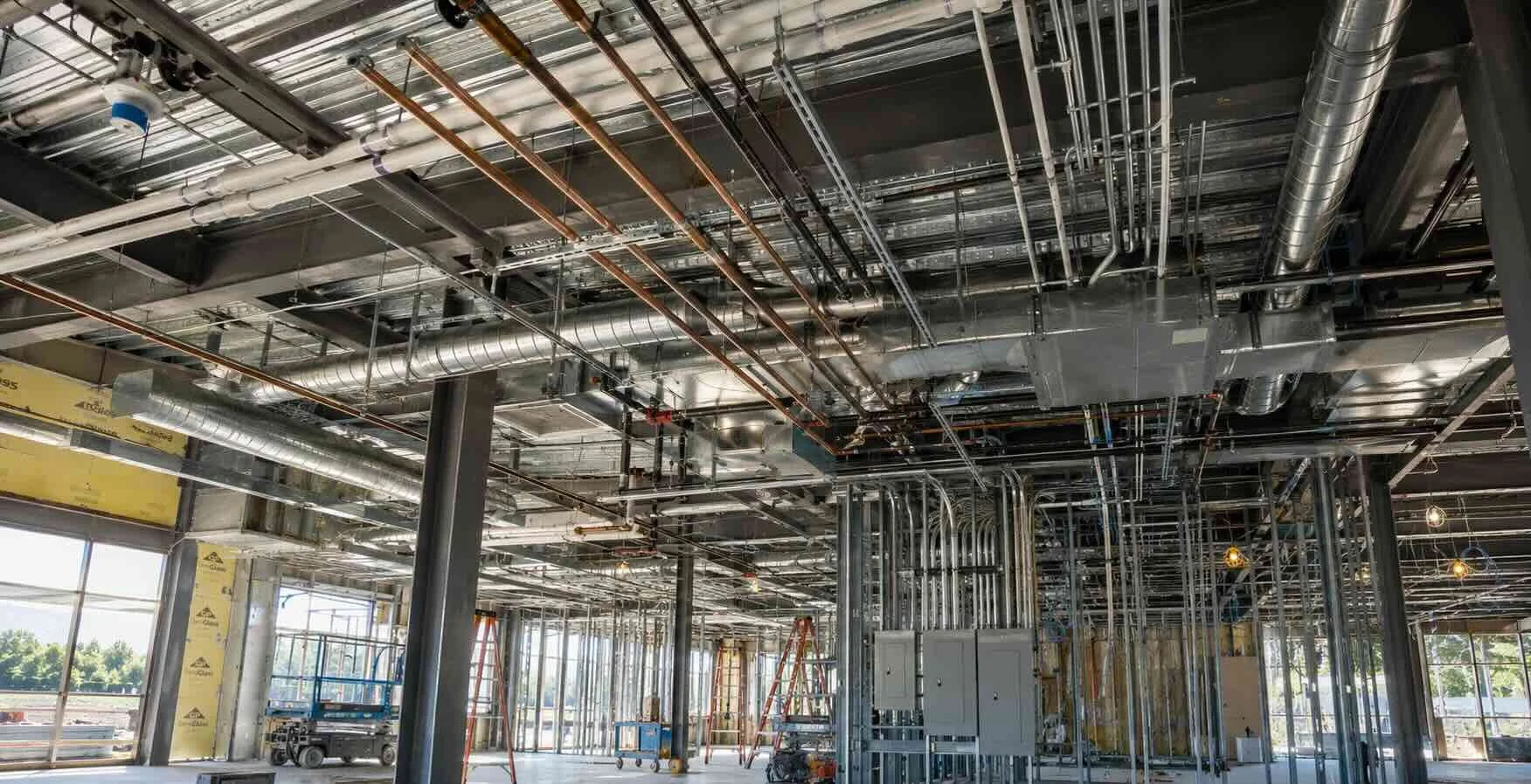 Exposed mechanical, electrical, and plumbing systems installed throughout a commercial building under construction.
