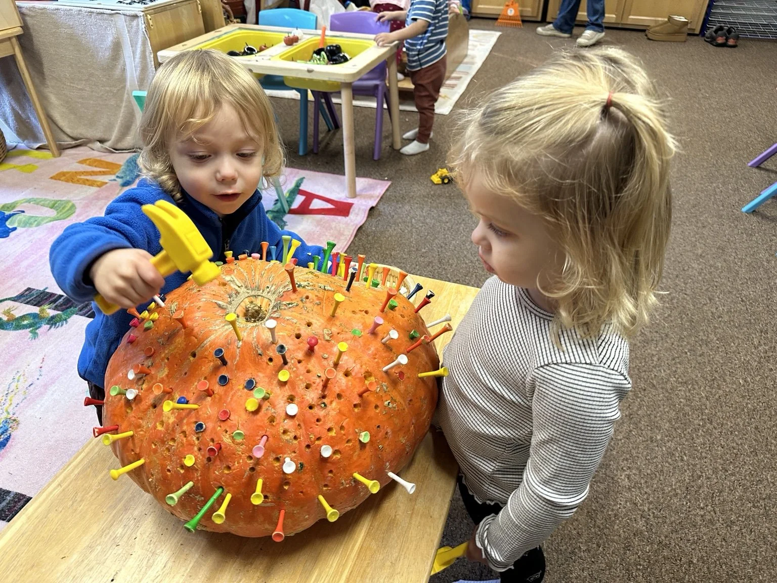 Children developing fine motor skills during a hands-on pumpkin activity.