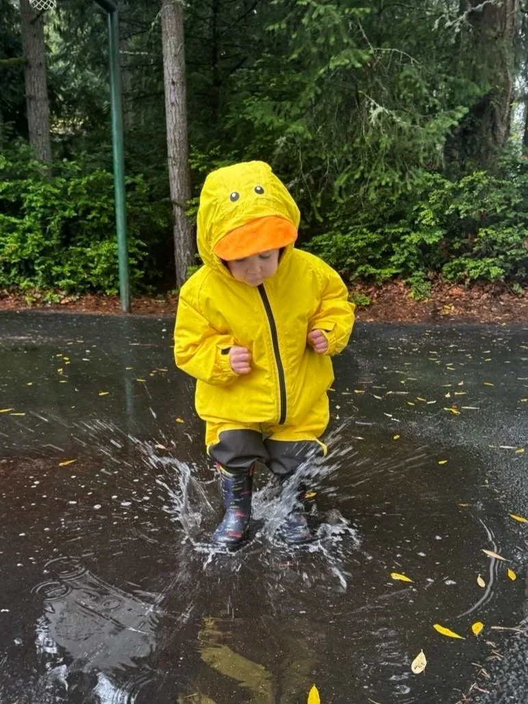 Child embracing outdoor play while exploring puddles in the rain.