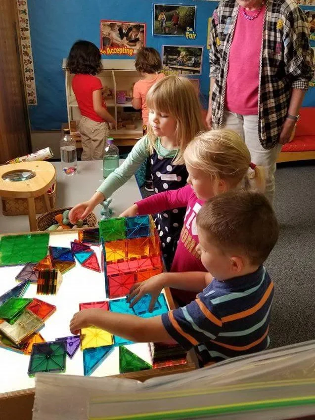 Children building and problem-solving with magnetic construction tiles.