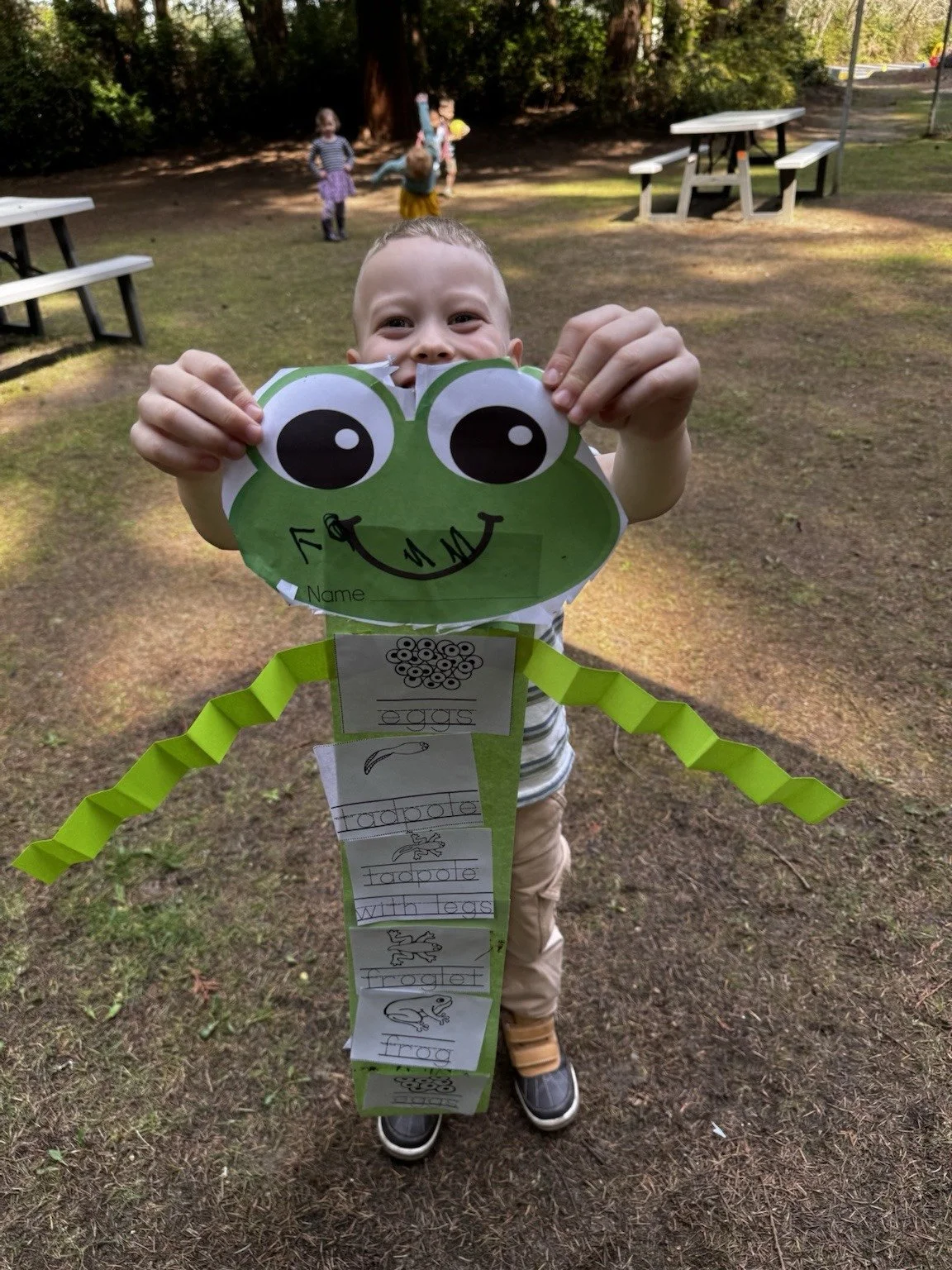 Child proudly showing a frog-themed craft during outdoor learning.