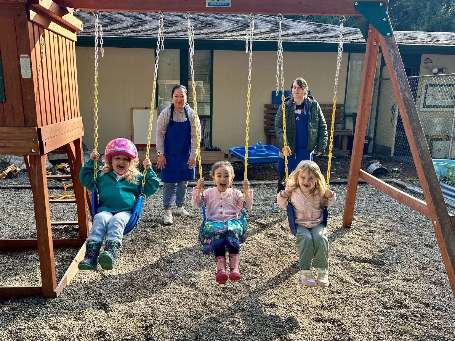 Children and parent volunteers enjoying swings on the outdoor playground.
