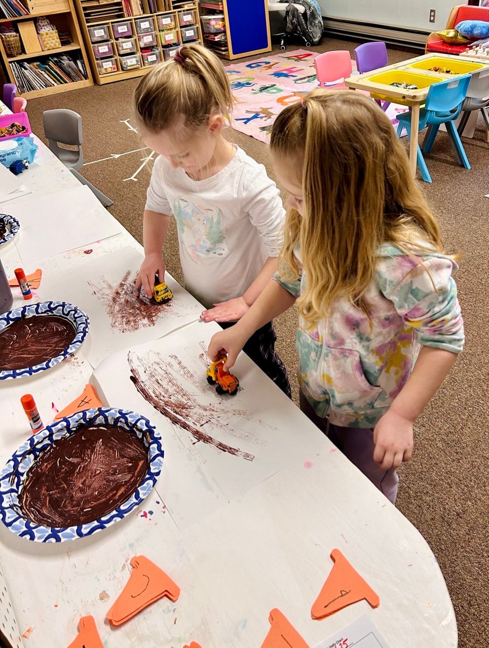 Children combining art and imaginative play with construction vehicles.