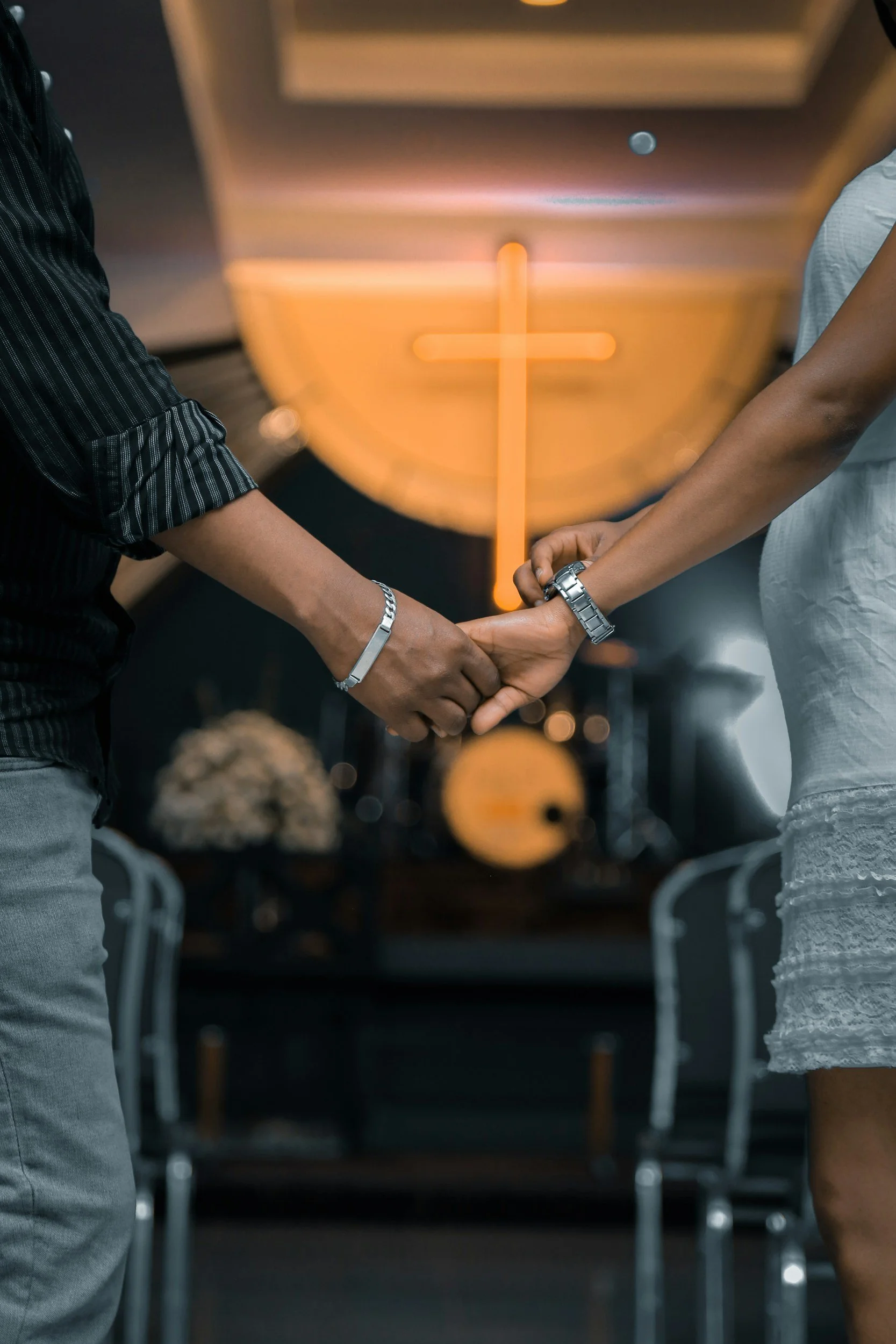 Deux personnes, un couple se tenant par la main lors d'une cérémonie, avec une croix en lumière orange en arrière-plan.