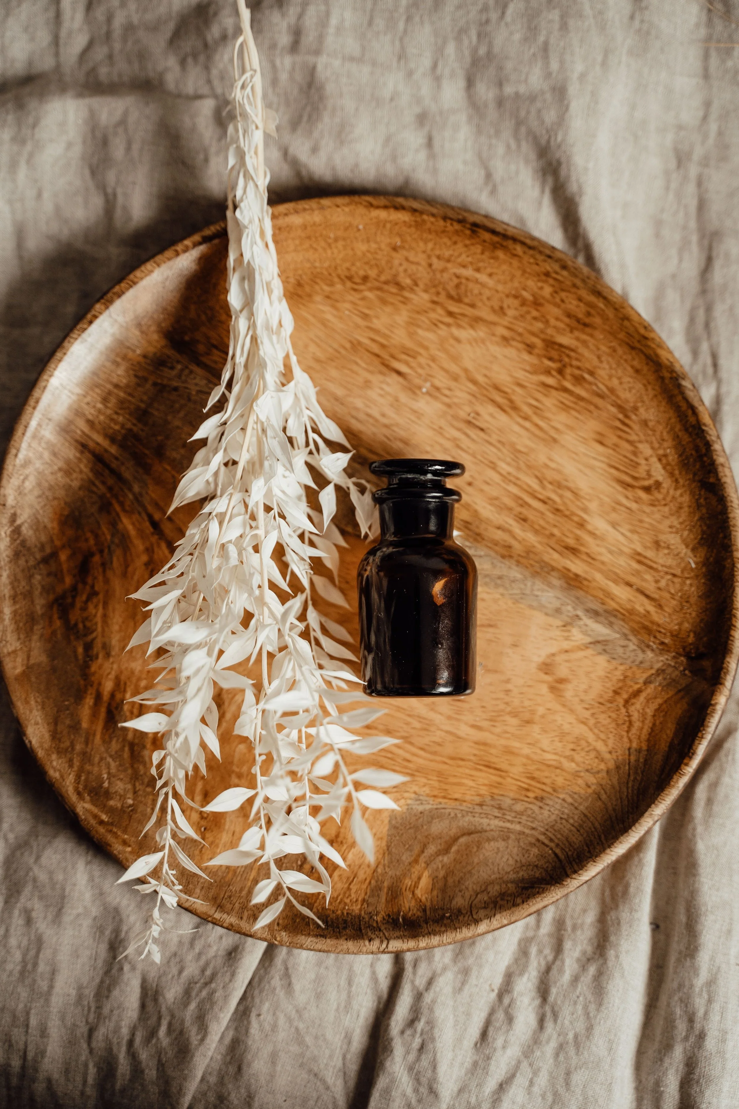 A wooden tray with a black bottle and a white decorative branch, placed on a beige fabric surface.