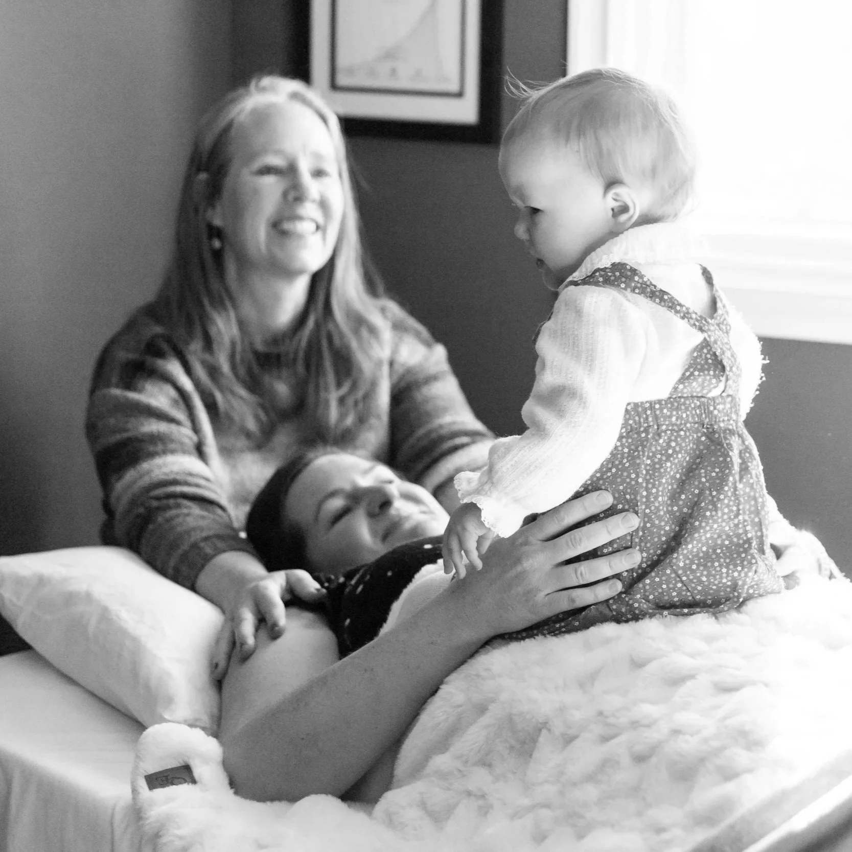 A woman, children, and a man gather around a bed, appearing to enjoy a joyful moment together.