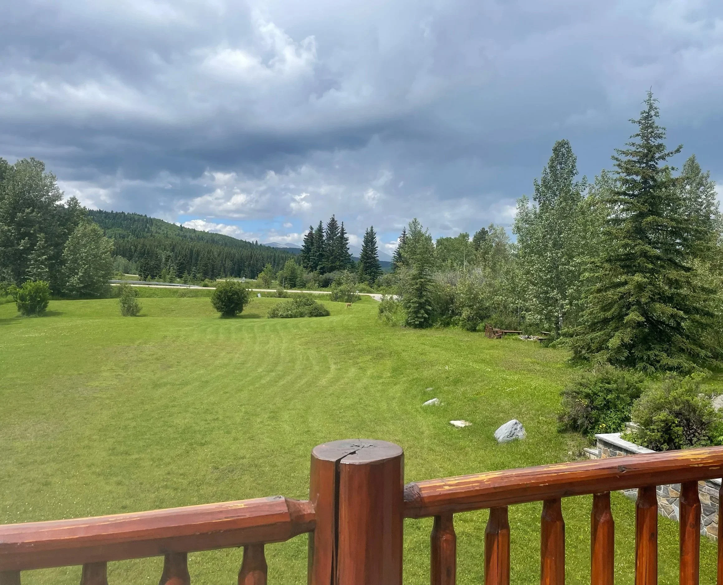 A scenic landscape with a green lawn, trees, and a cloudy sky over distant hills.