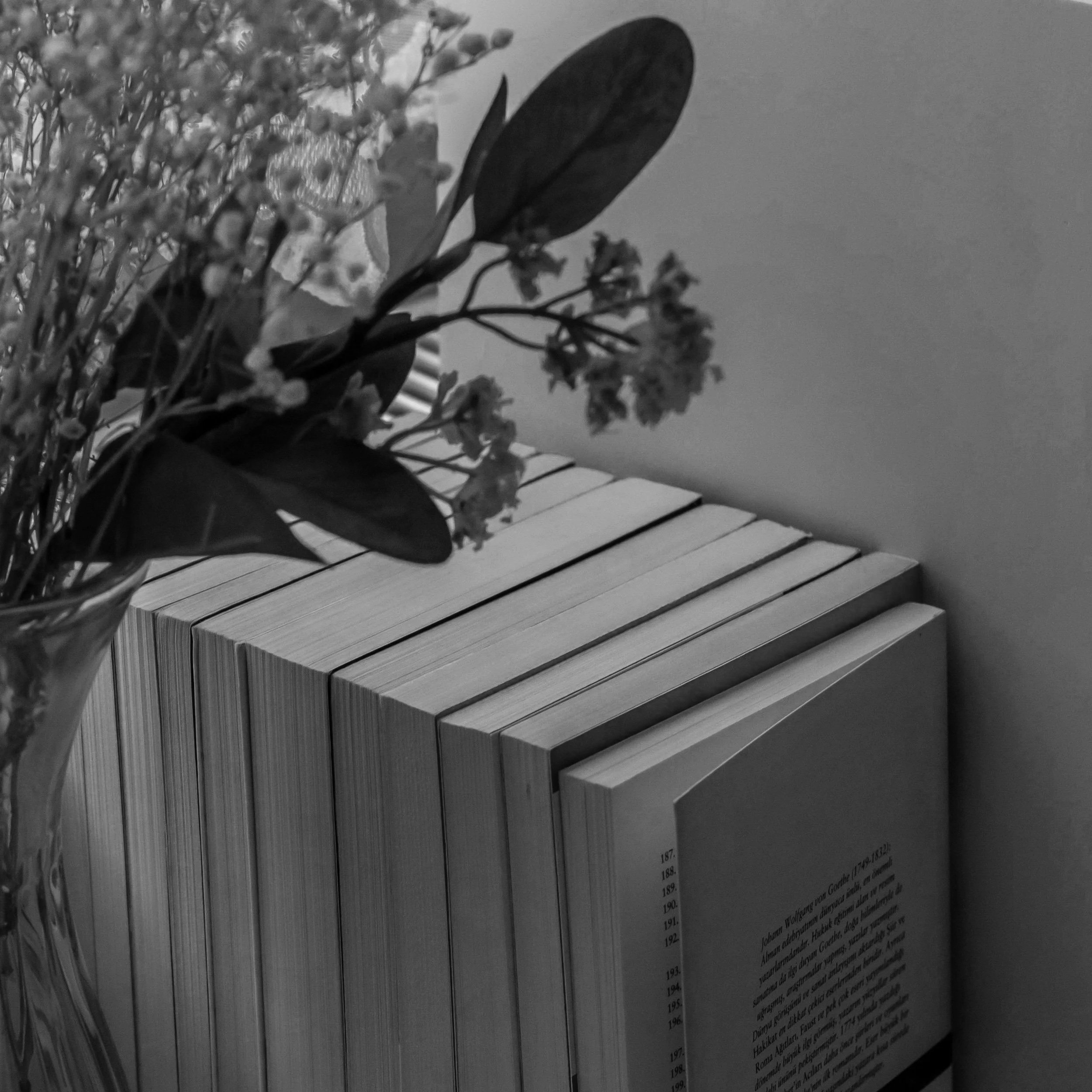 A vase of flowers sitting on a wooden piano, with part of a book or newspaper visible in the foreground.
