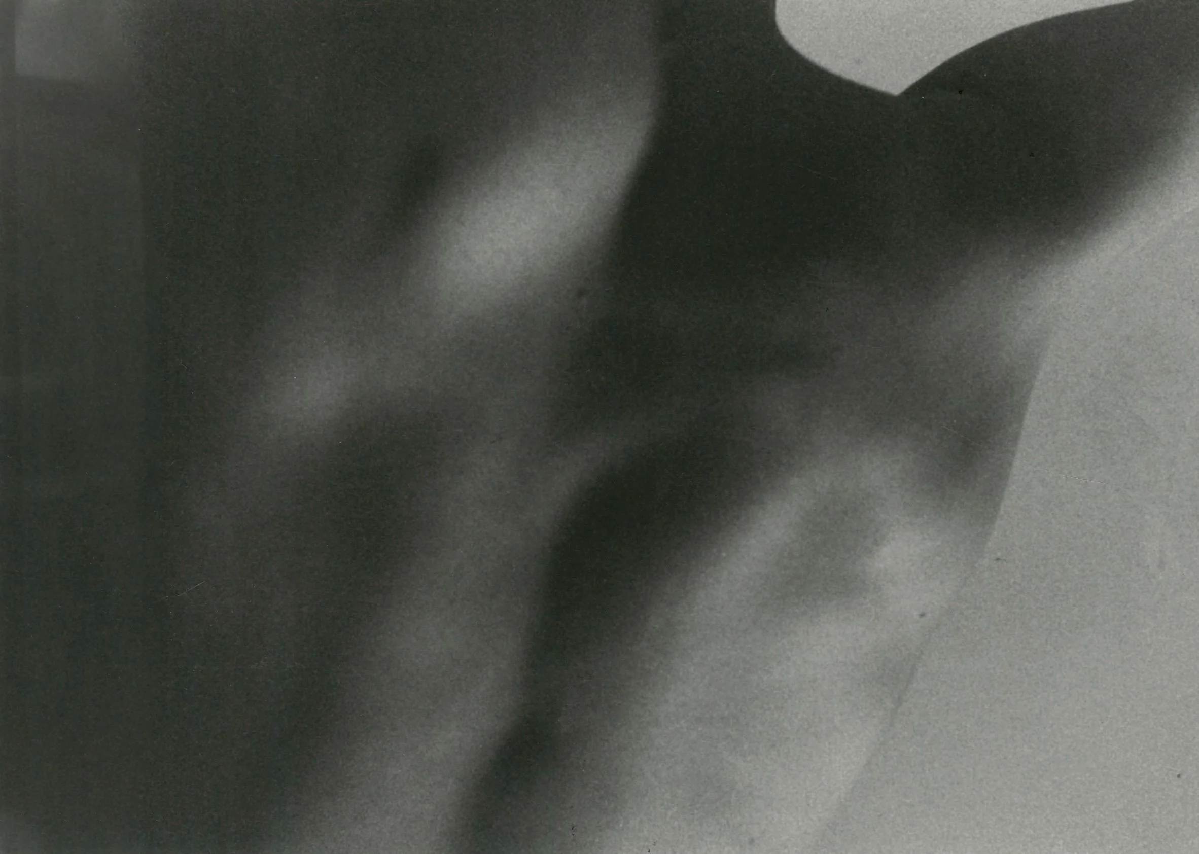 A blurry grayscale image of a person with their back turned, wearing a dark dress or shirt, in front of a light-colored background.