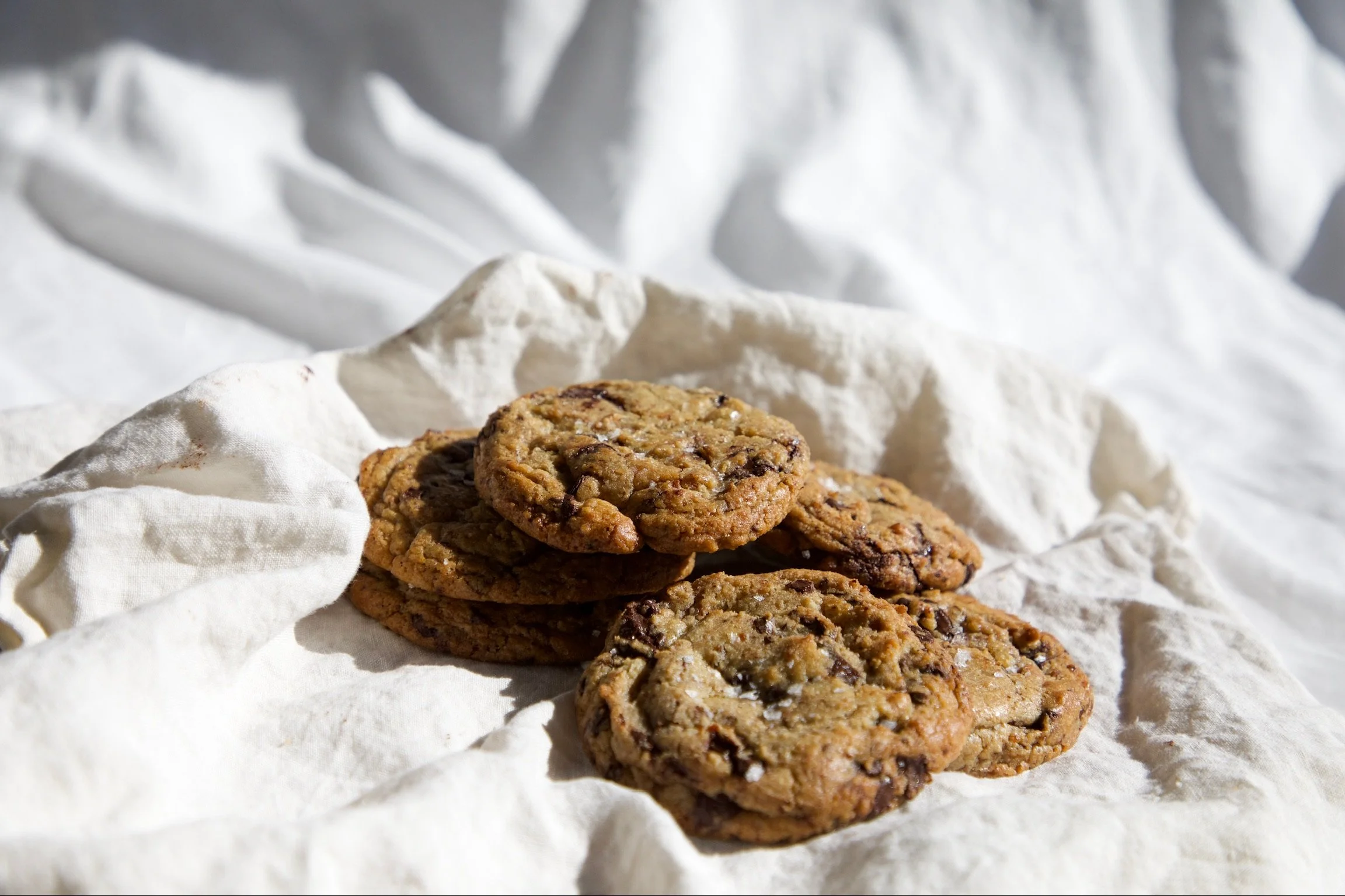 Stack of chocolate chip cookies on crumpled white paper.