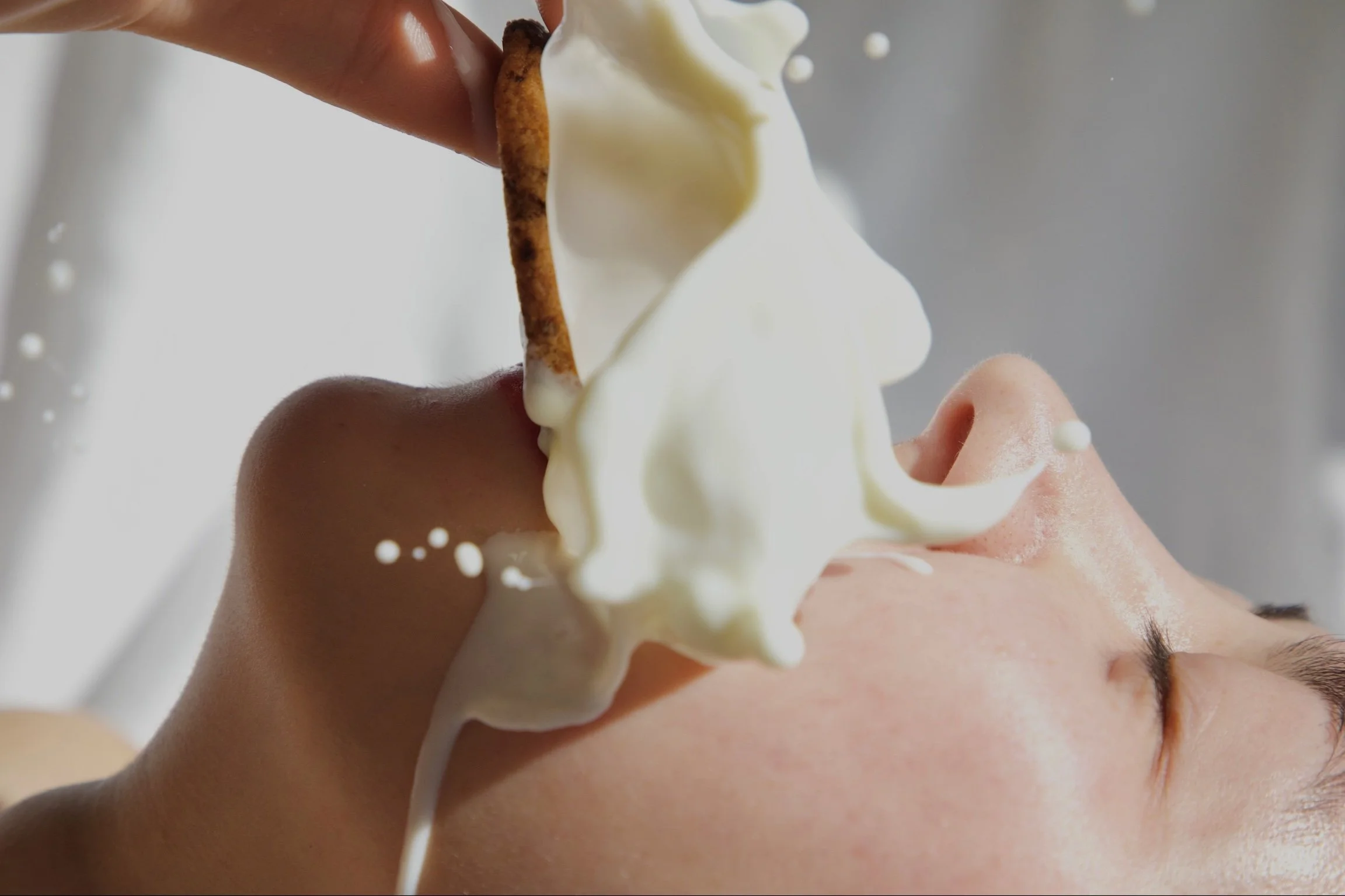 Close-up of a person with their eyes closed, face tilted upwards, and chocolate and vanilla ice cream being scooped onto their face.
