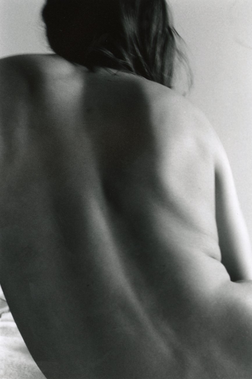 Black and white photograph of a person viewed from behind, showing their bare back and shoulder with dark hair.