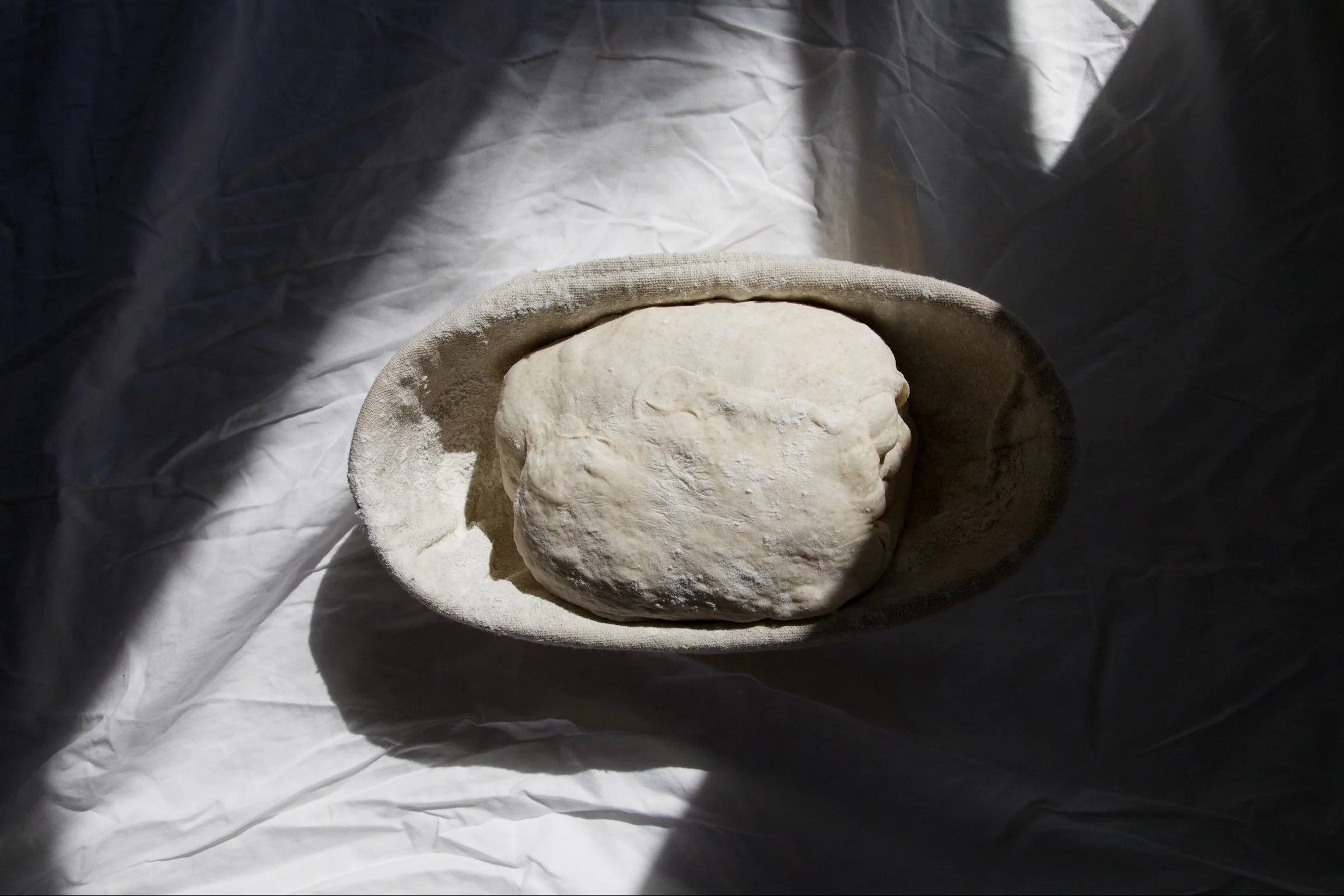 A round stone sculpture depicting a face, partially covered by a wide-brimmed hat, with surrounding white fabric.