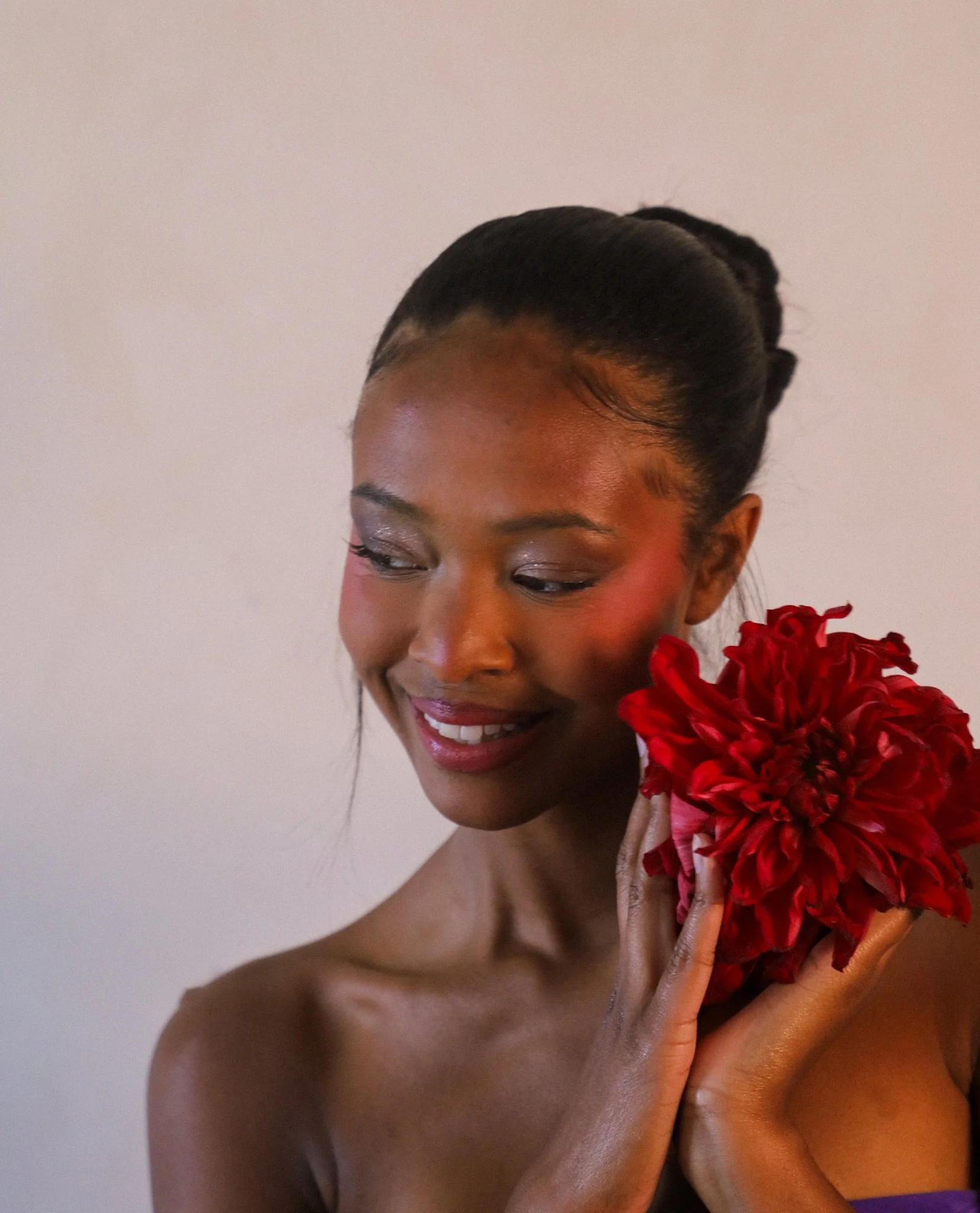 Close-up of woman with dark hair styled in an elegant updo, wearing floral accessories and makeup, smiling with eyes closed.