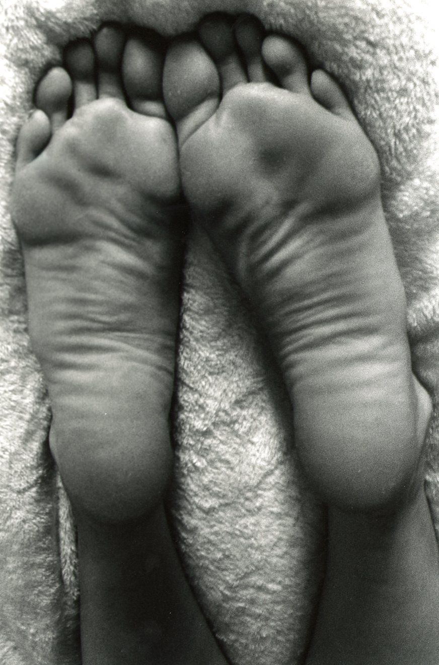 Close-up black and white photograph of two feet with toes curled inward, resting on a textured surface.