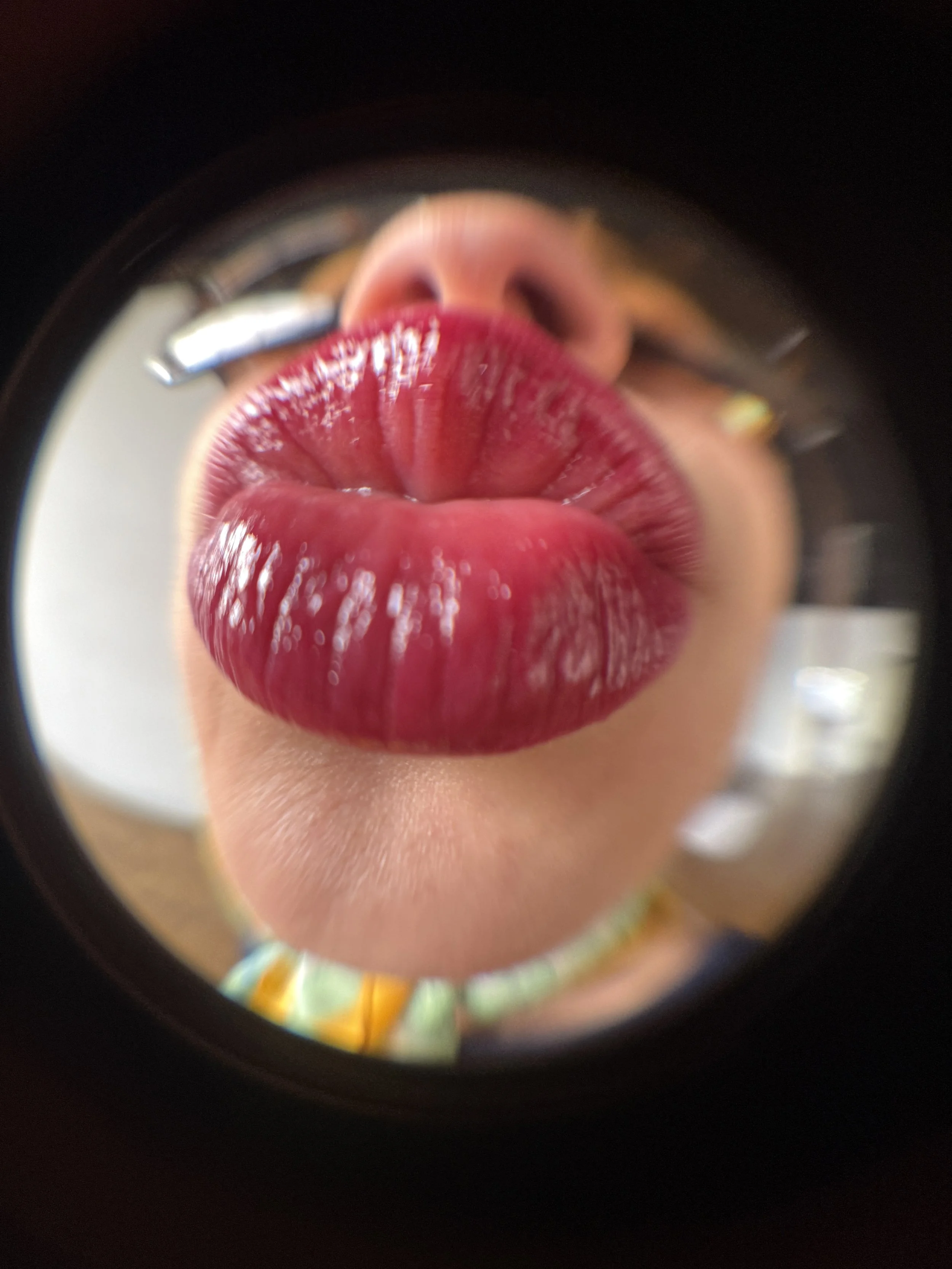 Close-up of a person with bright red lipstick, viewed through a circular mirror or lens, with blurred background.