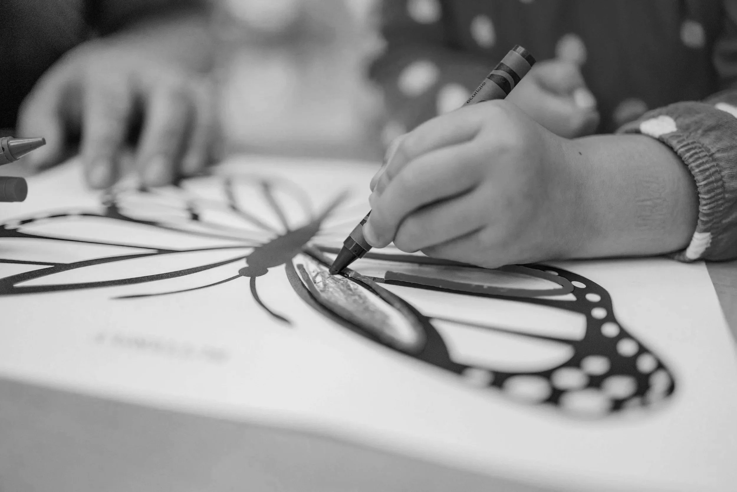 A person's hand holding a marker, drawing intricate black and white patterns on a sheet of paper.