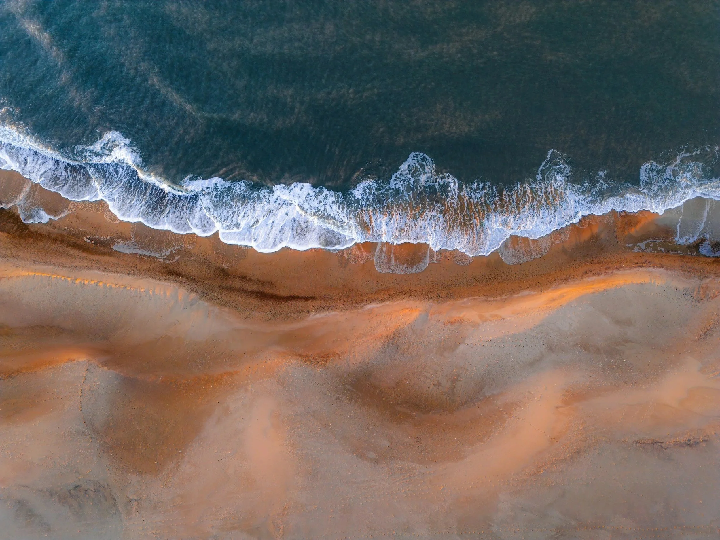 Aerial view of the ocean with white waves crashing on the sandy beach.
