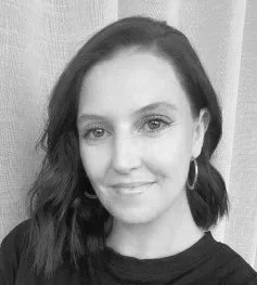 Black and white photo of a woman with shoulder-length hair, wearing hoop earrings and a dark top, smiling at the camera.