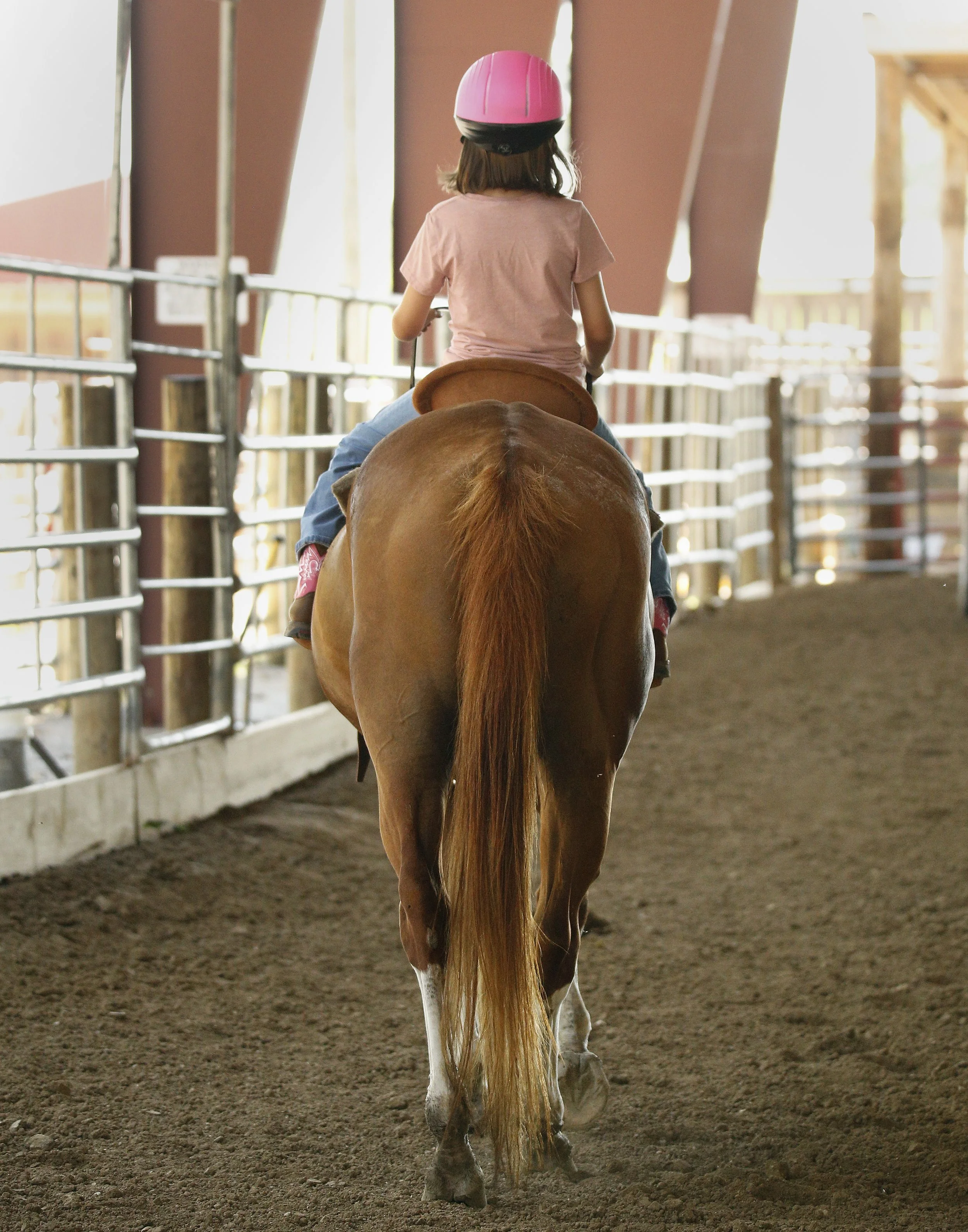 A girl riding a horse away from the camera
