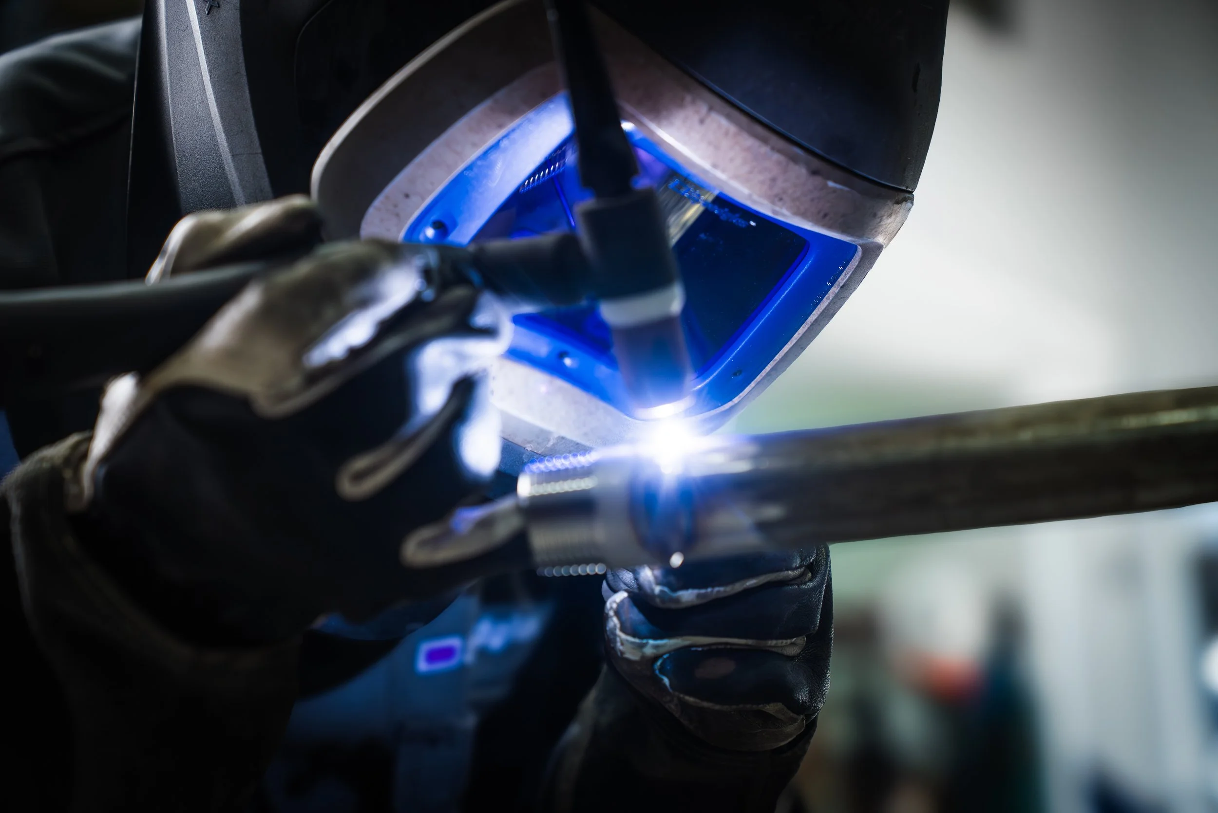 A welder wearing gloves welding metal with bright blue light in a workshop.