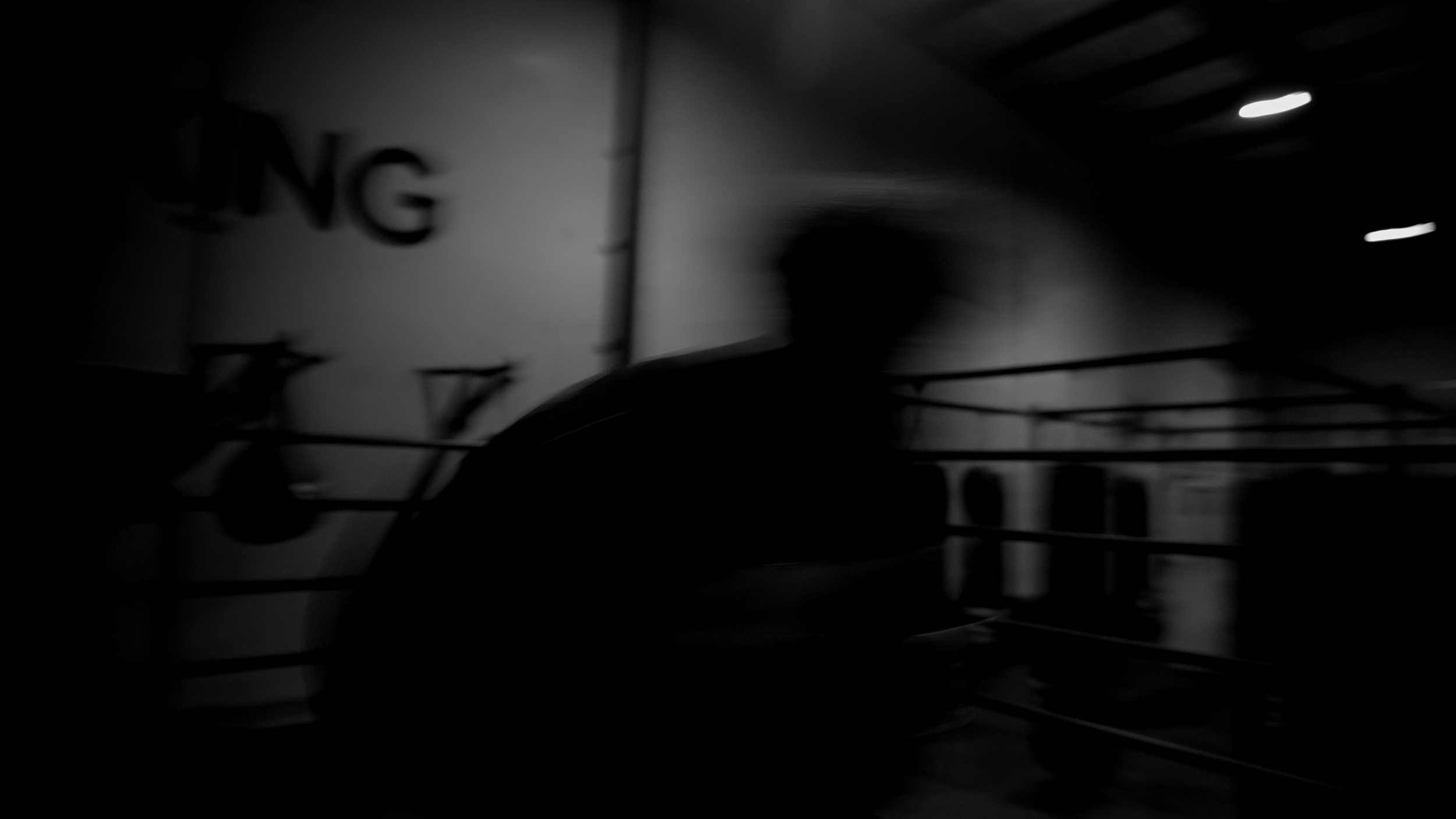A dimly lit underground parking garage with a silhouette of a person walking, and blurred structural elements and signage in the background.