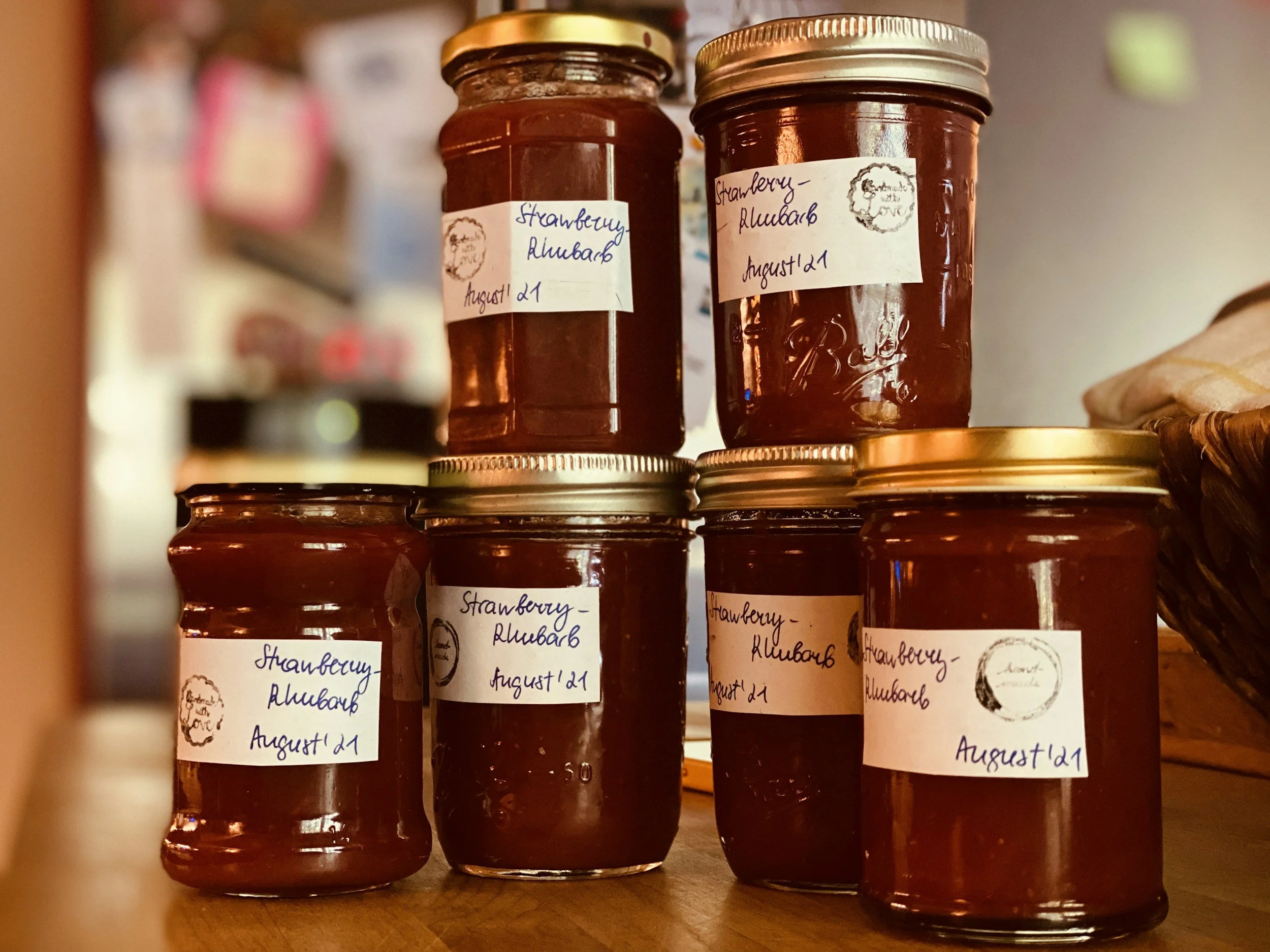 Jars of strawberry rhubarb jam with handwritten labels dating August 21, placed on a wooden surface.