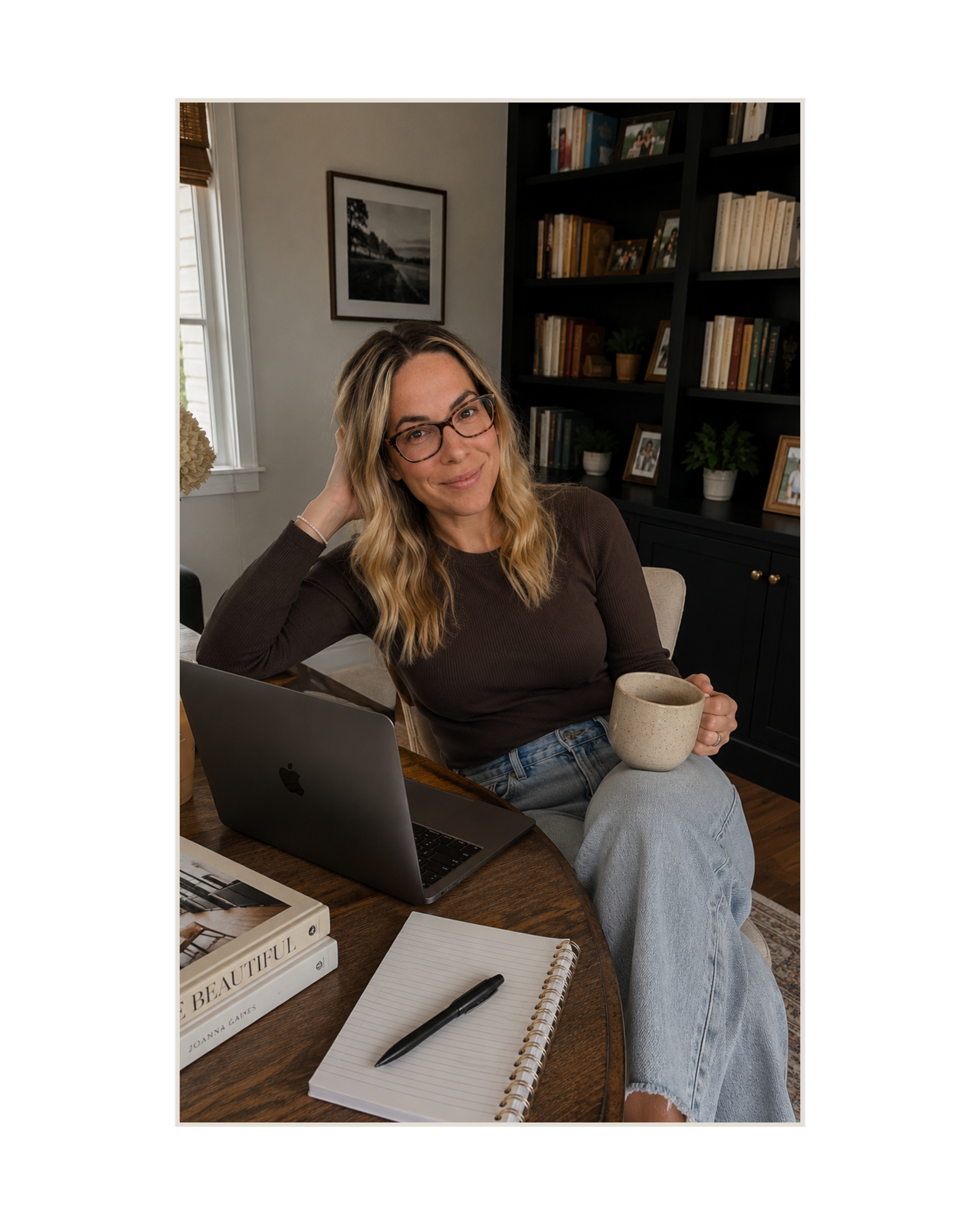 Haus of Whit Brand Photoshoot 2026. Whitney Radacina sitting at a wooden desk in a room with a bookshelf, holding a beige mug, with an open laptop, a notebook, and a pen in front of her.