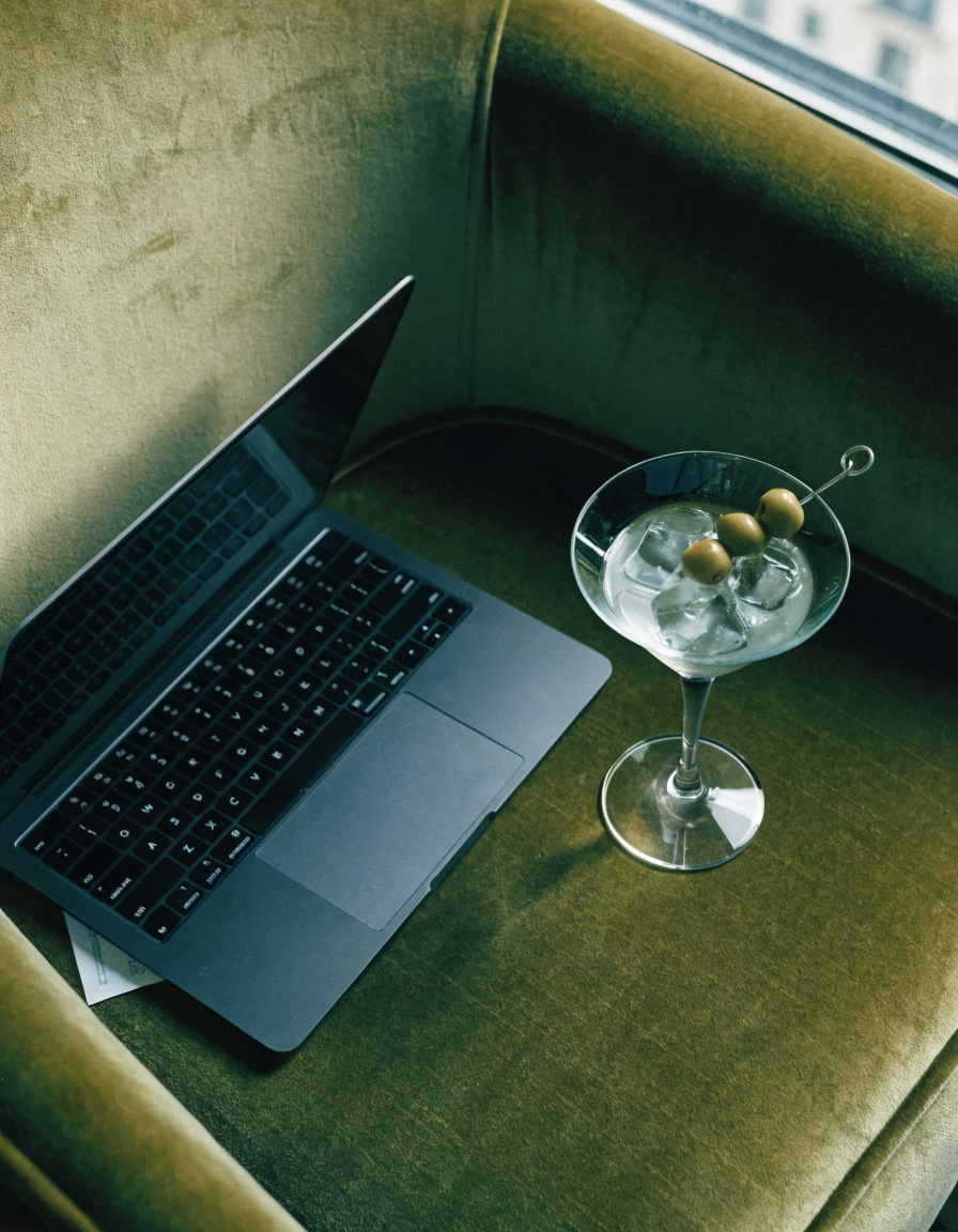Haus of Whit, Whitney Radacina Brand Photoshoot 2026.  A green velvet chair with a laptop and a cocktail glass filled with ice and green olives.