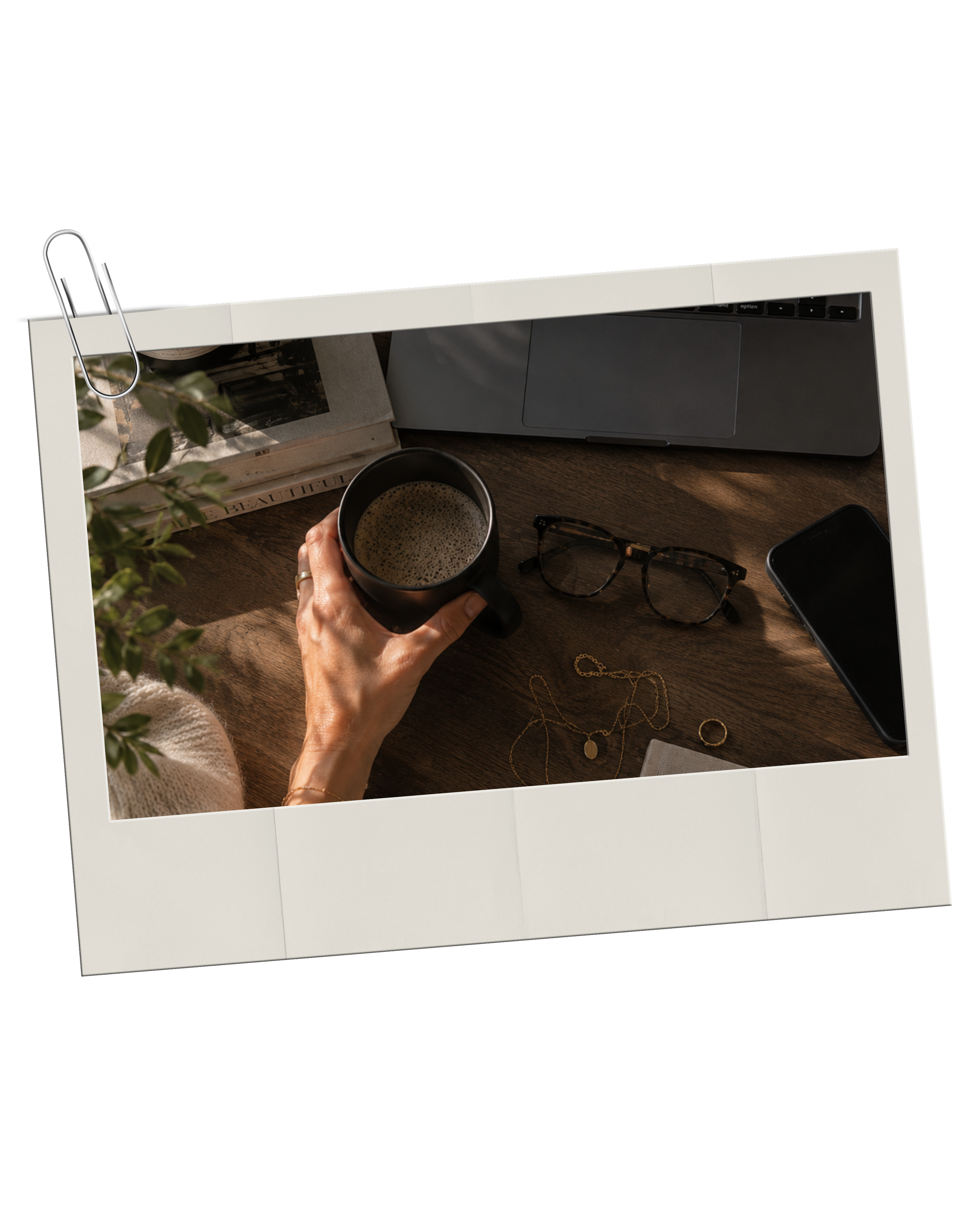 Haus of Whit Brand Photoshoot 2026. Flat lay of Whitney Radacina holding a cup of coffee at a wooden desk with eyeglasses, jewelry, a notebook, and a smartphone, with a laptop and decorative items nearby.