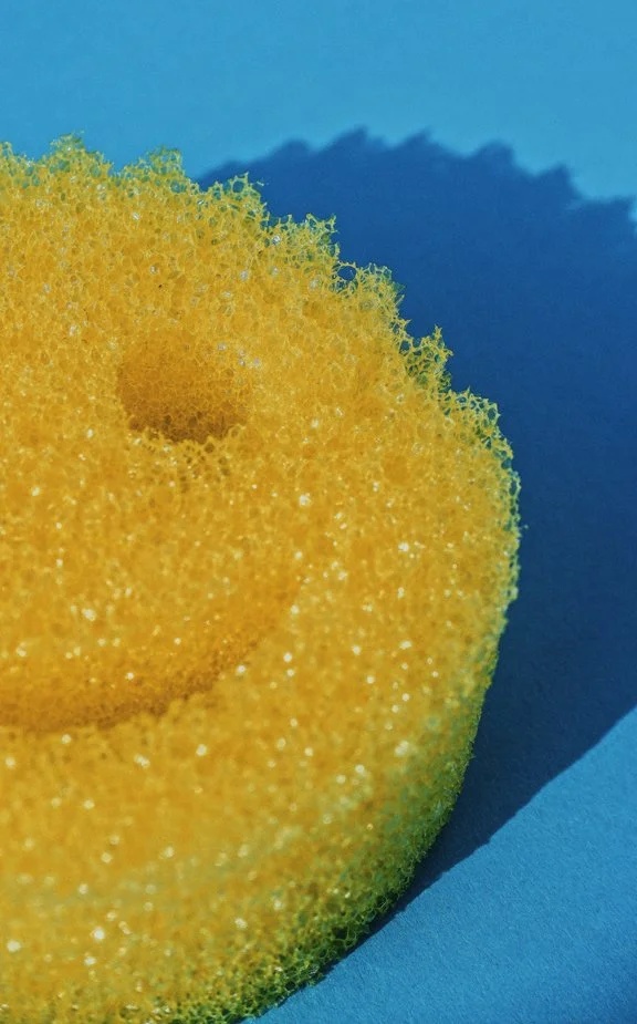 Close-up of a yellow kitchen sponge with a porous texture, placed on a blue surface.