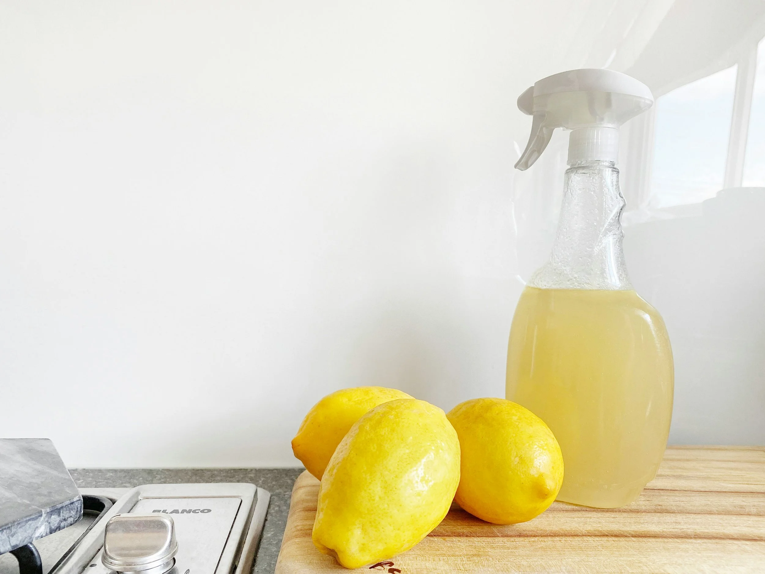 Lemonade bottle, lemons, and a scale on a kitchen counter with a white wall in the background.