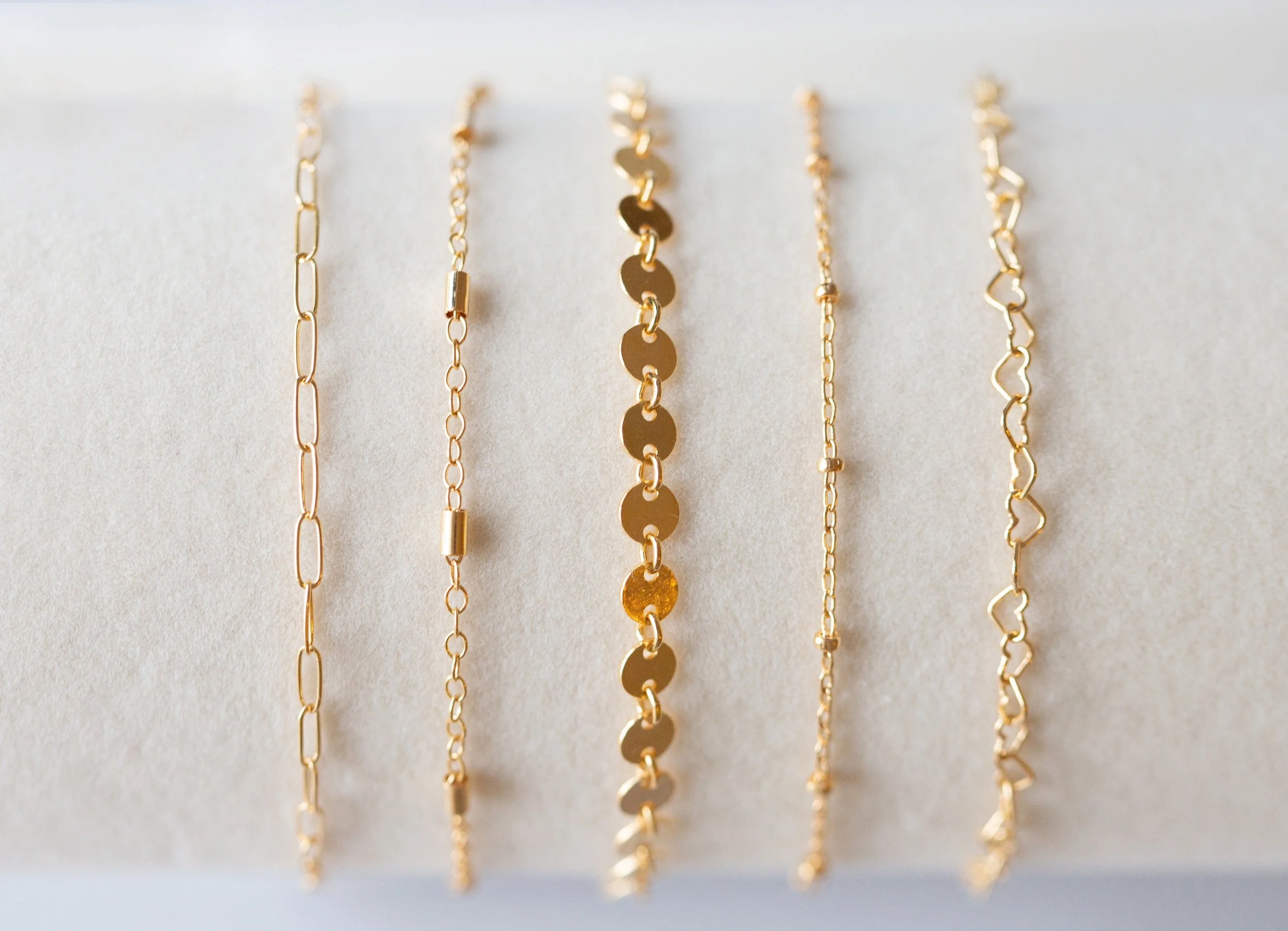 Close-up of five gold chain necklaces with different link styles, hanging on a white surface.