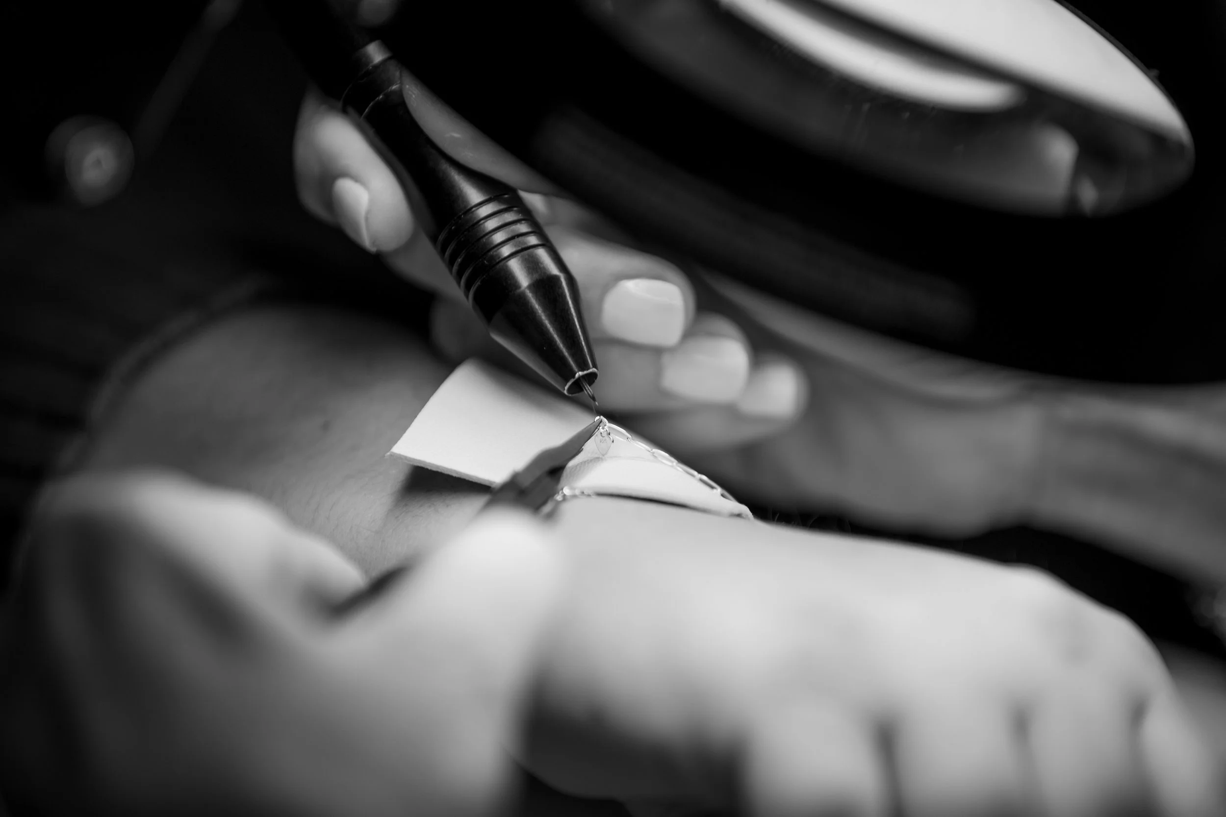 A close-up black and white photo of a hand holding a Permanent Jewelry machine from Avec Toi Permanent Jewelry.