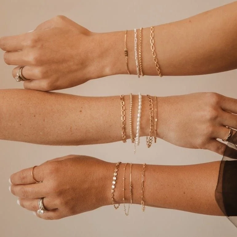 Three arms with various gold and pearl jewelry, including bracelets and rings, displayed against a plain background.