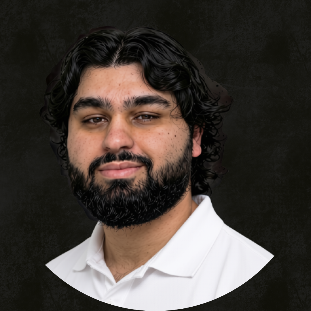 A young man with dark, wavy hair, a beard, and wearing a white shirt against a dark background.