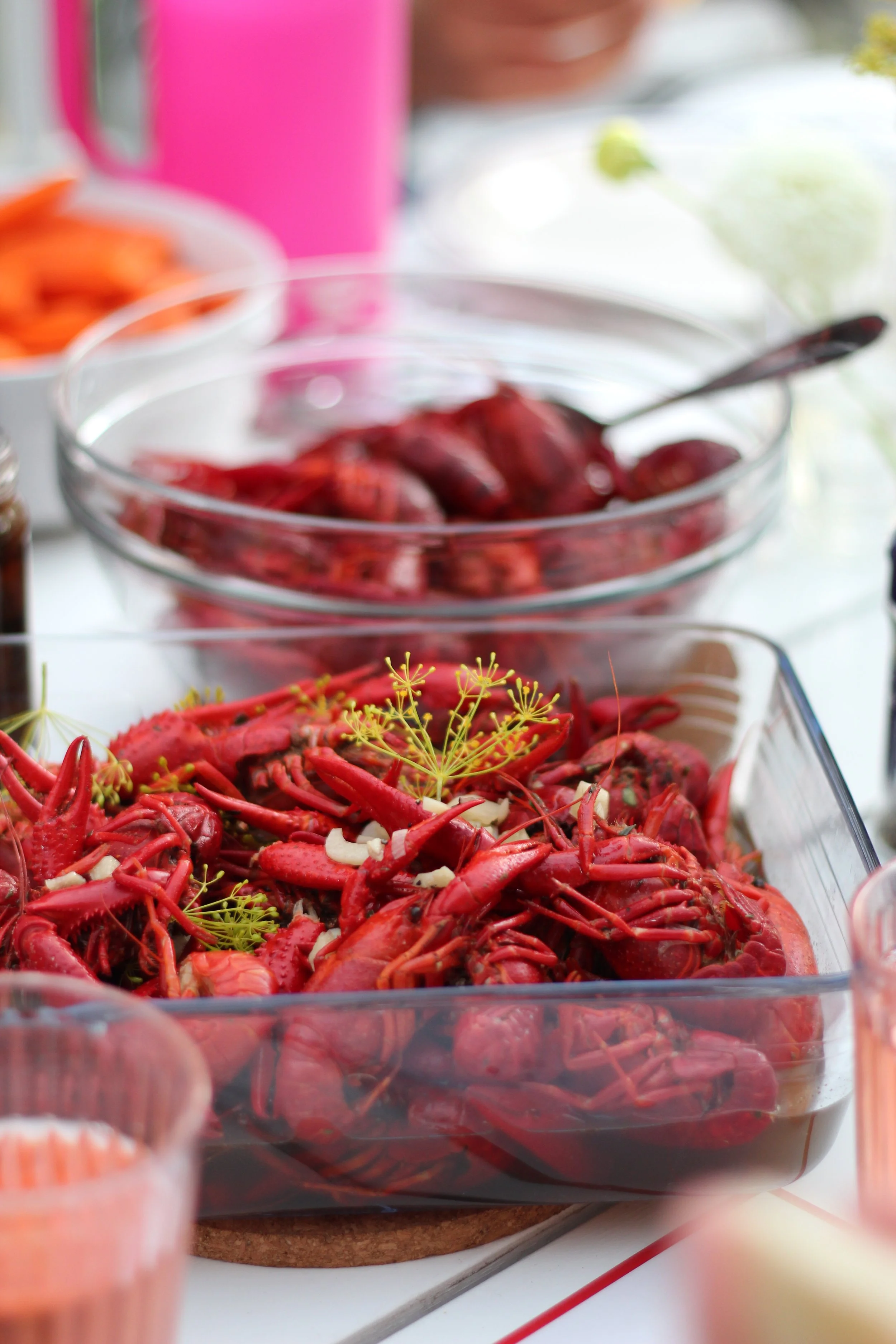 A bowl of cooked crawfish with herbs and garlic, with other dishes and a person in the background.