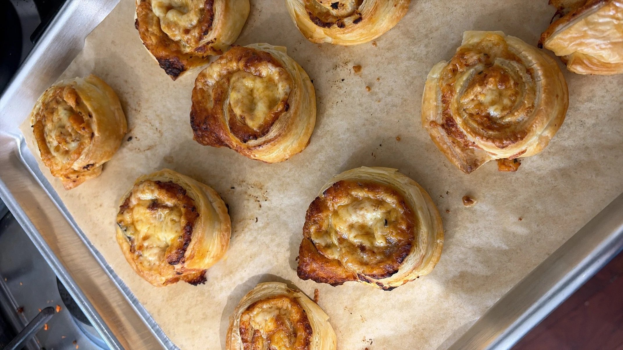 Baked pastry pinwheels with cheese and possibly ham or bacon, arranged on a baking sheet lined with parchment paper.