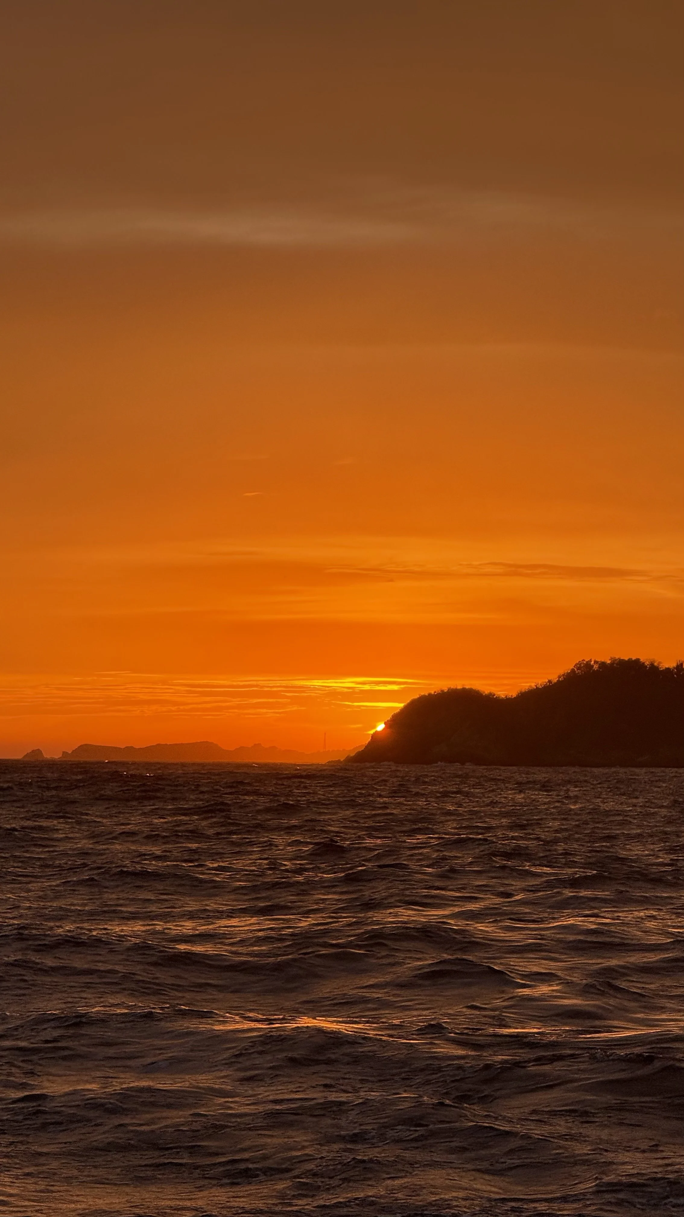 Atardecer sobre el mar con una isla en el horizonte y un cielo anaranjado con nubes dispersas.
