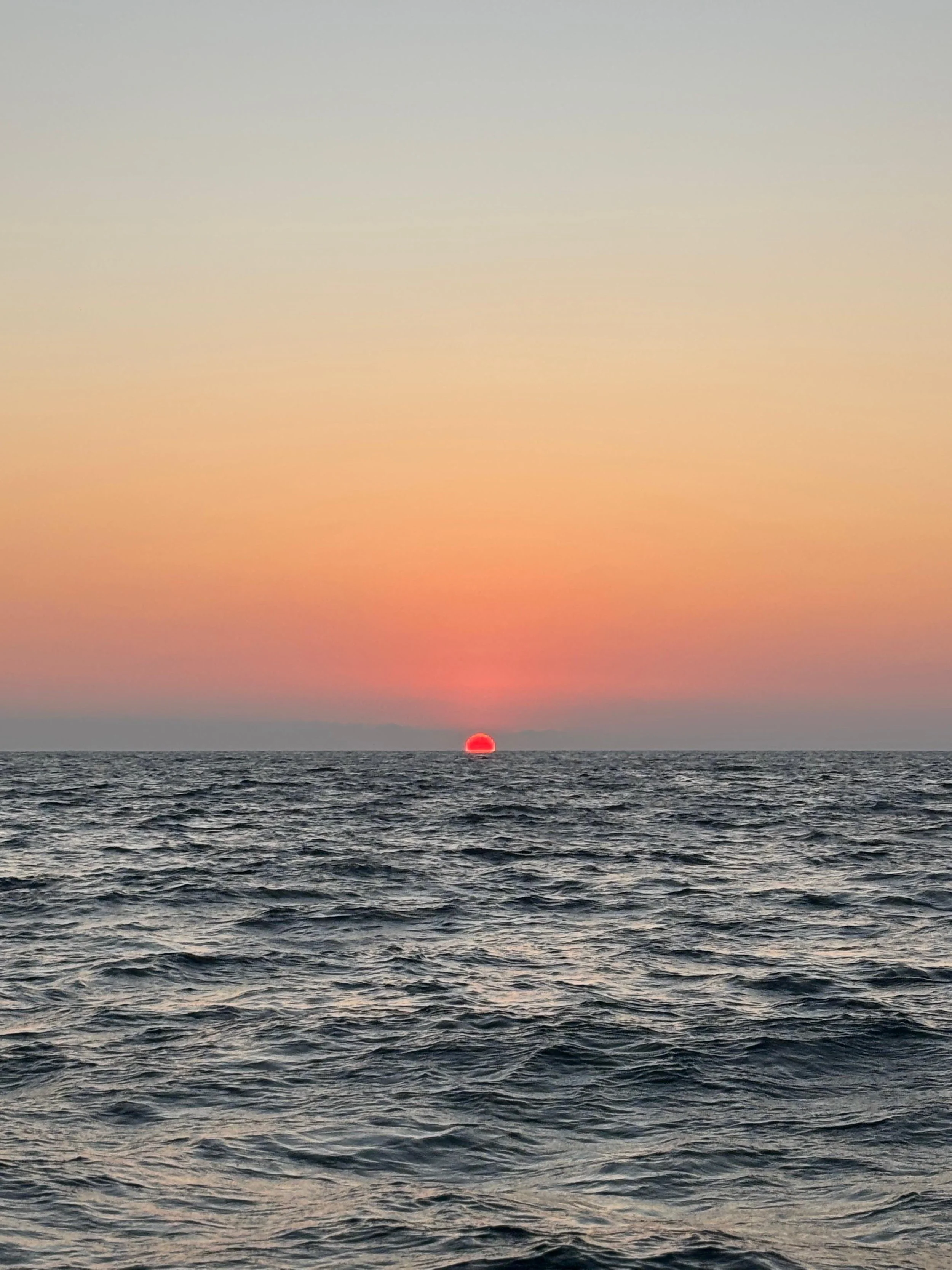 Atardecer en el océano con el sol en el horizonte y olas en la superficie del agua.