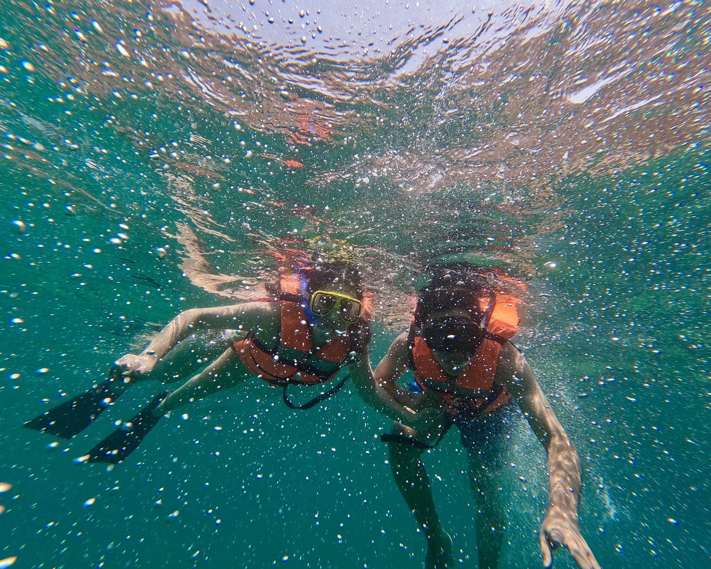 Persona con máscara de snorkel y gafas de buceo debajo del agua, rodeada de burbujas y azul profundo.