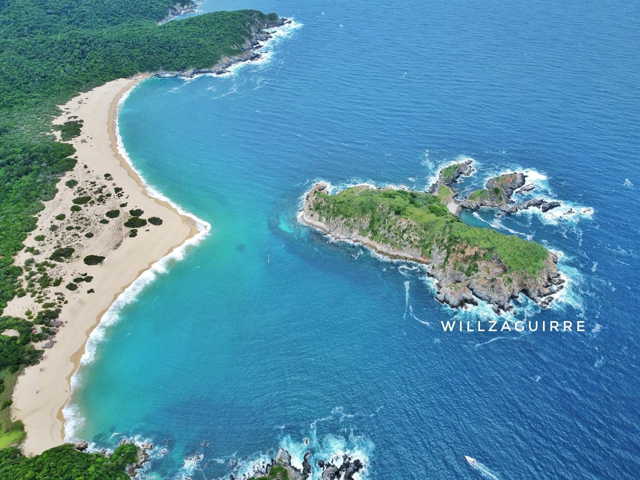 Costa con playa de arena blanca, agua turquesa y vegetación verde, formaciones rocosas en el mar y una pequeña isla
